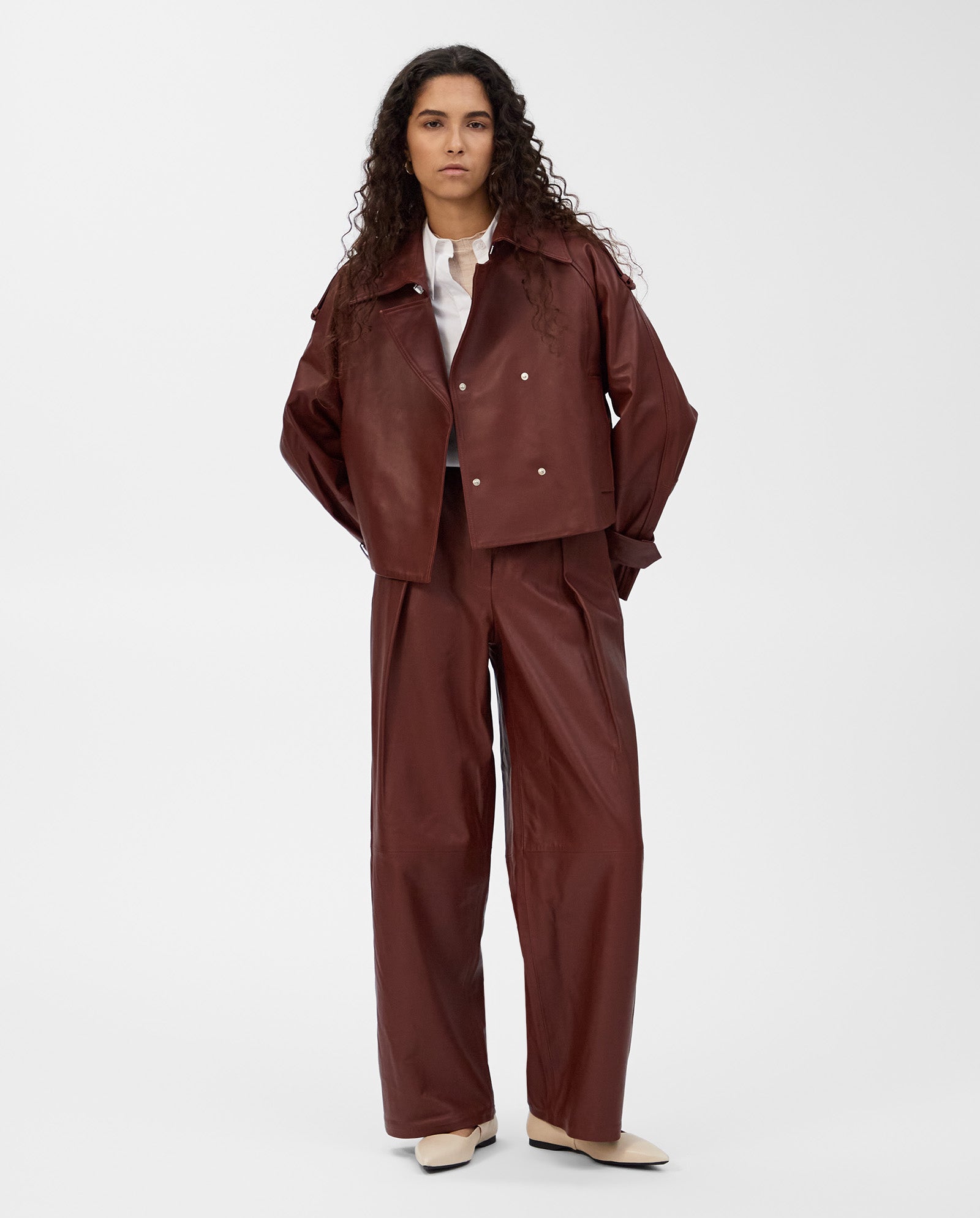 A person wears the brown IVY OAK LILITH ANN Jacket with a large collar and wide-leg pants, paired with a white top and cream shoes, standing against a white background.