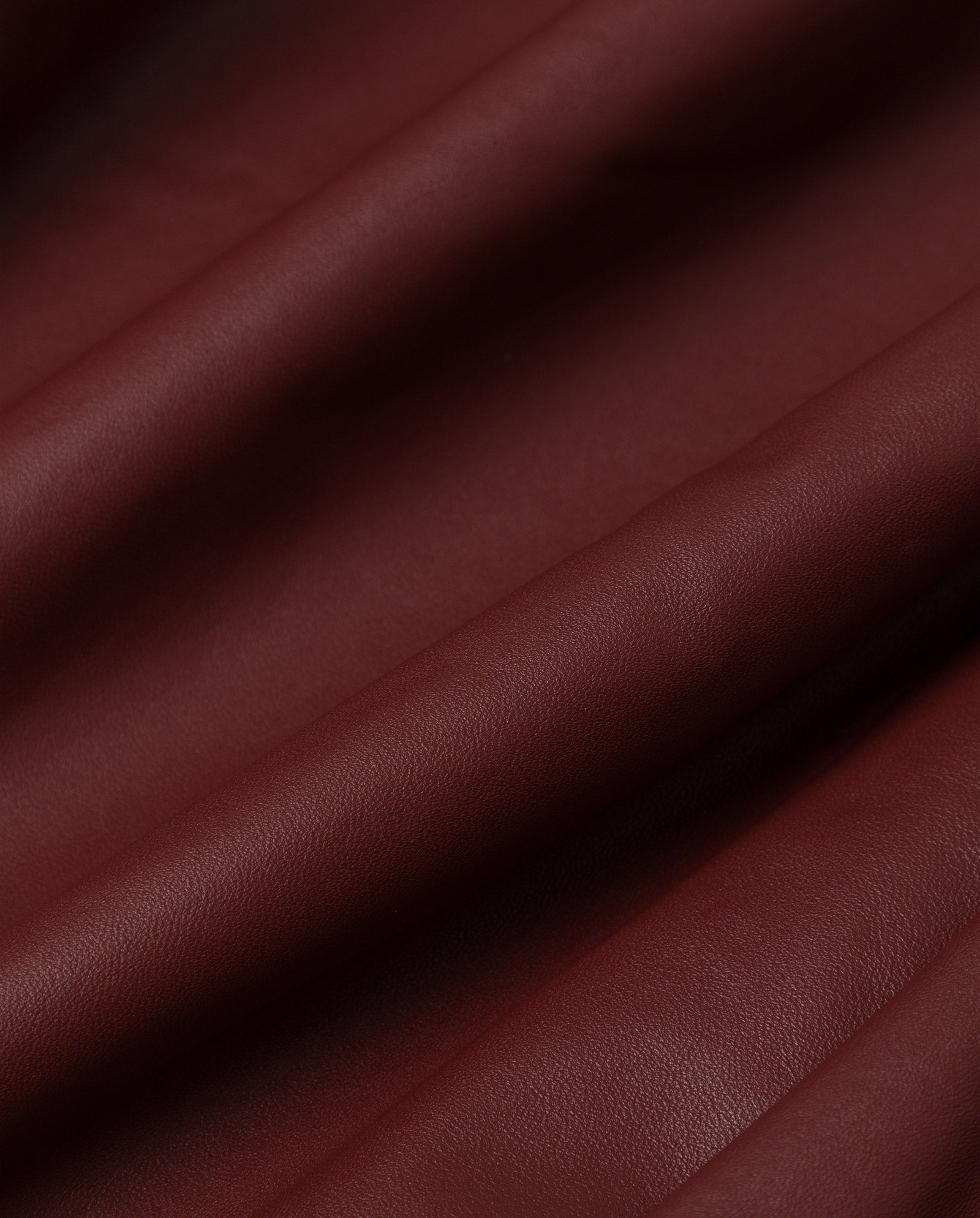 Close-up of maroon, textured leather fabric with soft folds and gentle shadows—perfect for an IVY OAK LILITH ANN Jacket or a statement trench coat with a large collar.