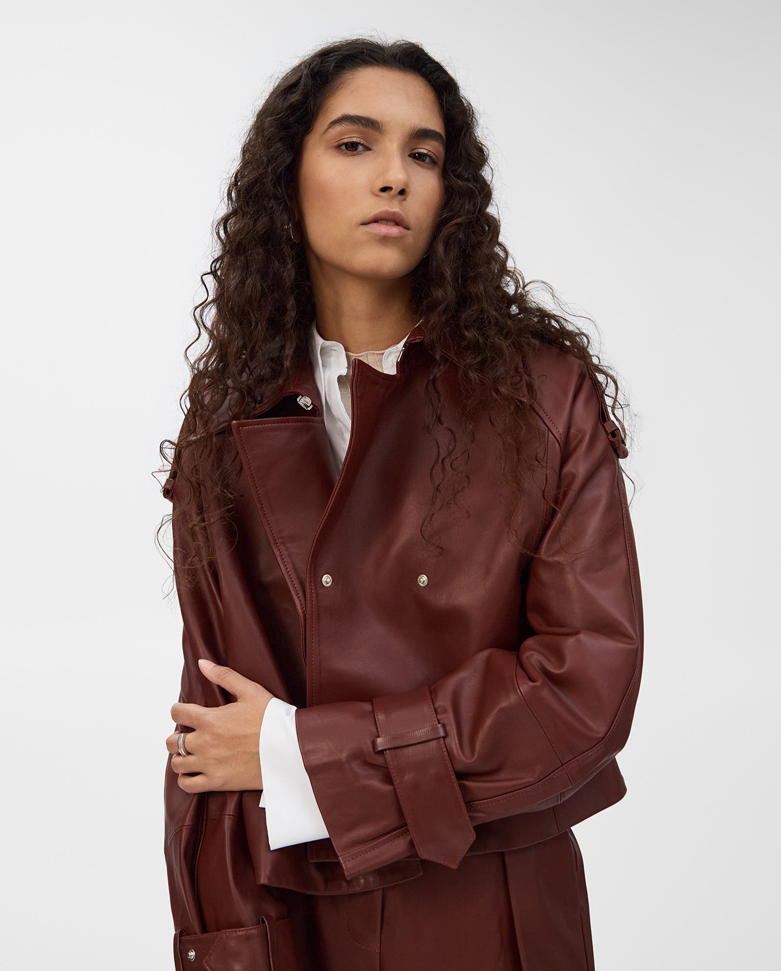 A woman with long curly hair poses confidently in a brown IVY OAK LILITH ANN Jacket with a large collar, layered over a white shirt.