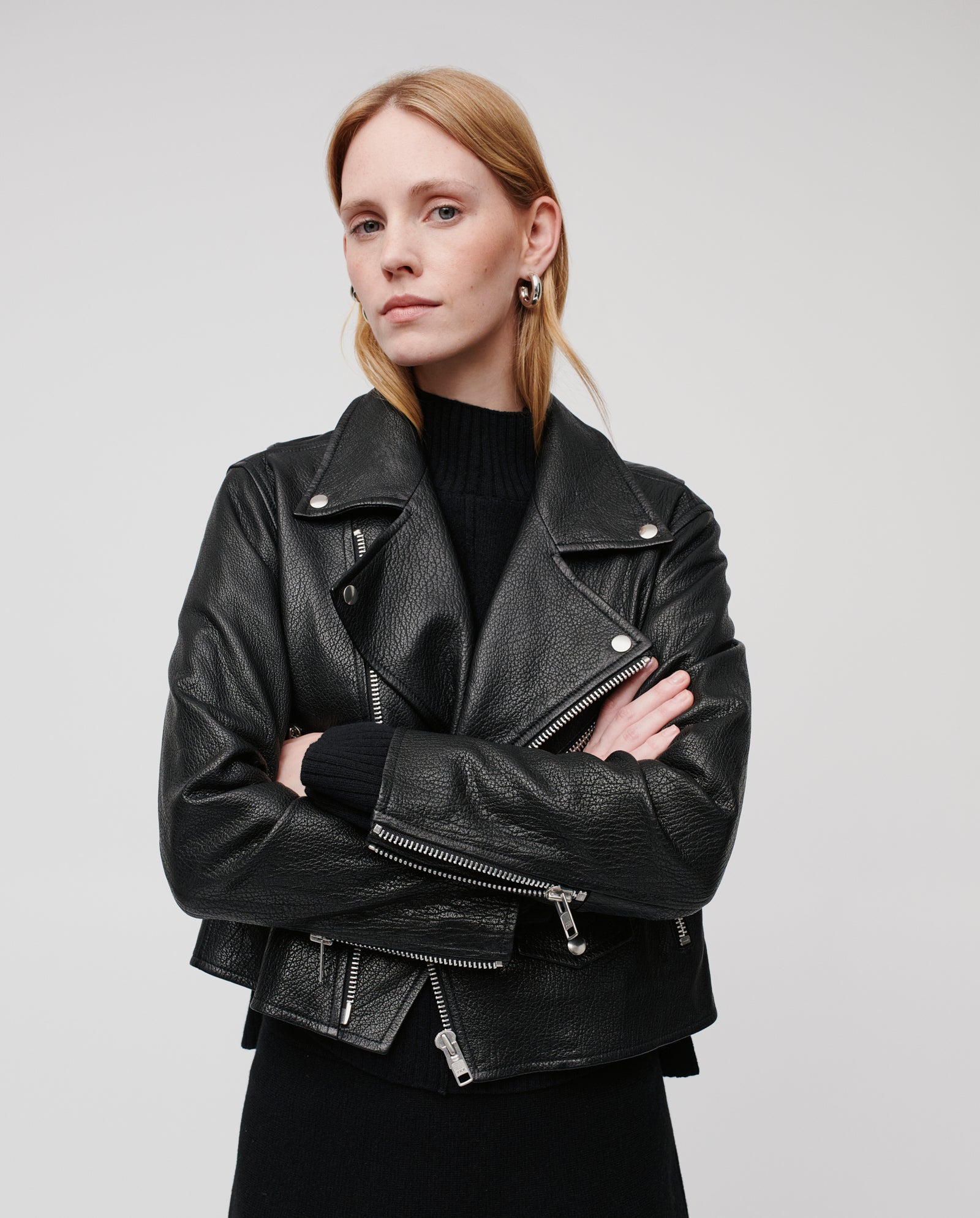 A woman with straight blonde hair wears the LENNY SUE Jacket by IVY OAK, crafted from chrome-free tanned leather, and stands with arms crossed against a plain background.