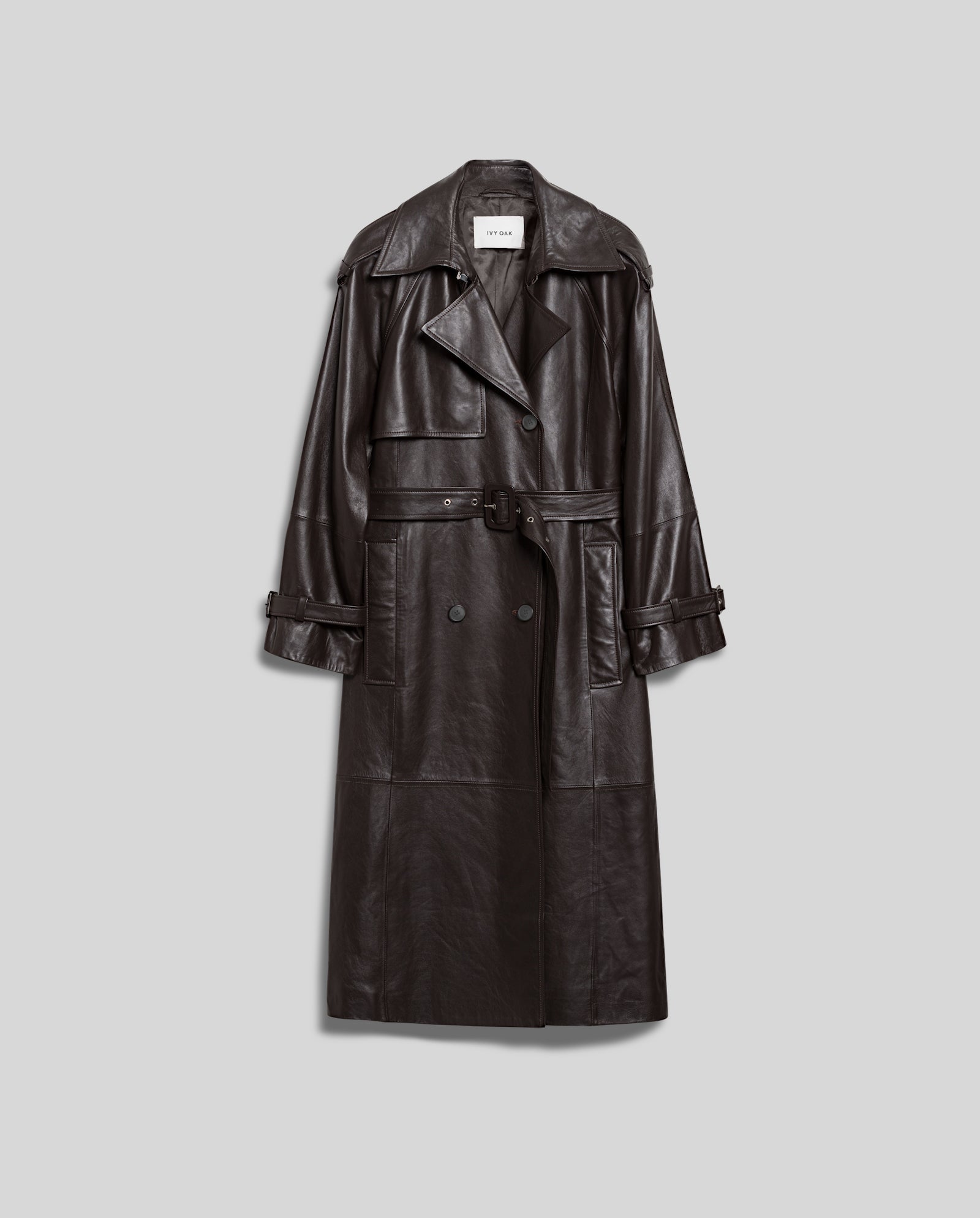 The LINDA Coat by IVY OAK is a long, black, oversized leather coat with a belt and double-breasted buttons, shown on a gray background.