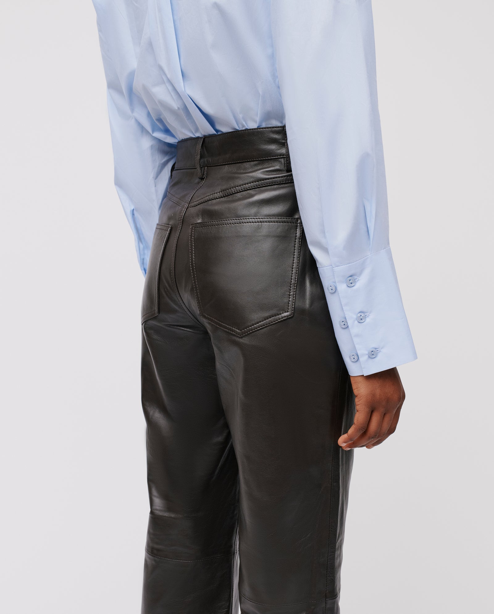Person wearing a light blue shirt and IVY OAK LINDSEY high-waisted black leather trousers, shown from the back with hand by their side.