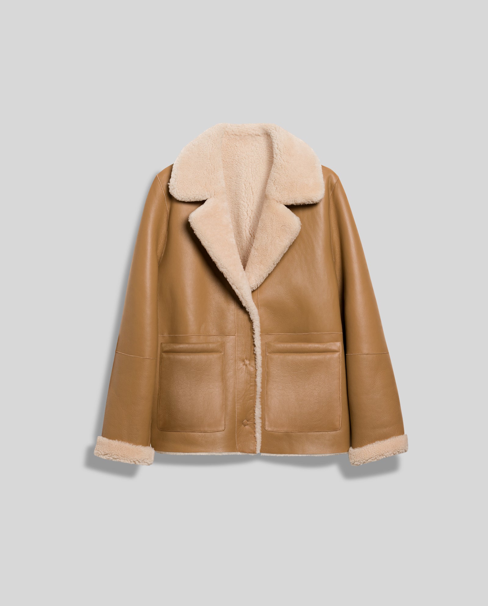 The LOTTE Jacket by IVY OAK is a light brown boxy shearling jacket with large lapels, front pockets, and a soft cream-colored lining, perfect for winter. Shown against a gray background.