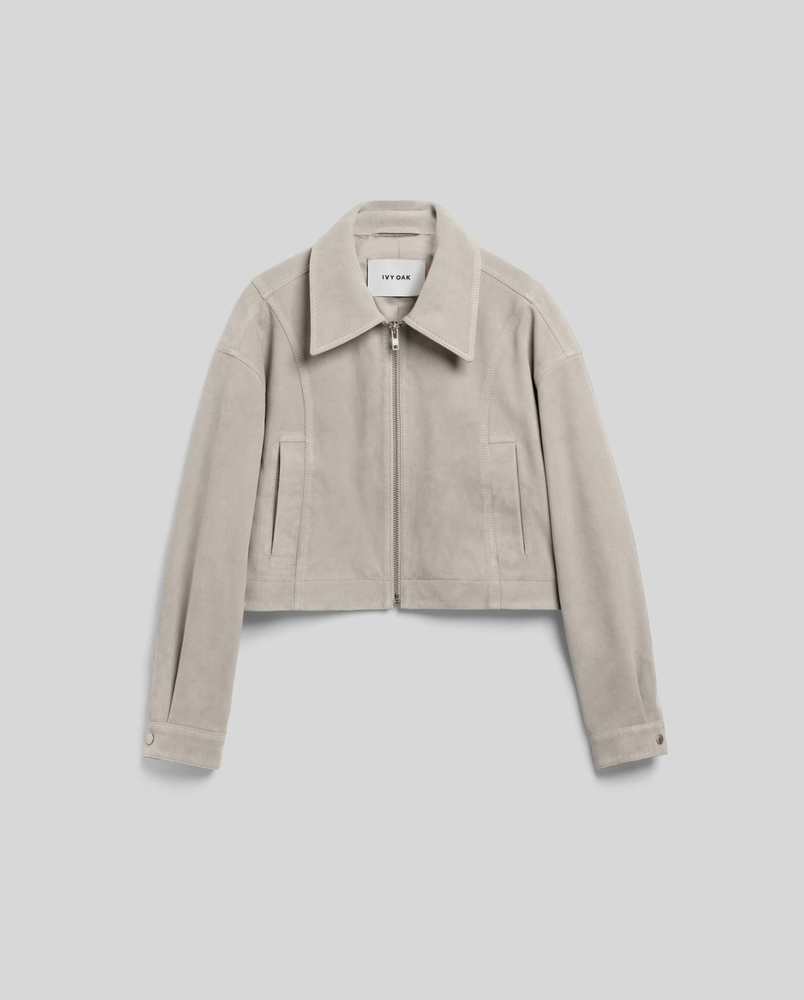 The LENA Jacket by IVY OAK is a light grey suede bomber with a front zipper, collar, wide sleeves, and a cropped boxy fit, shown laid flat on a plain background.
