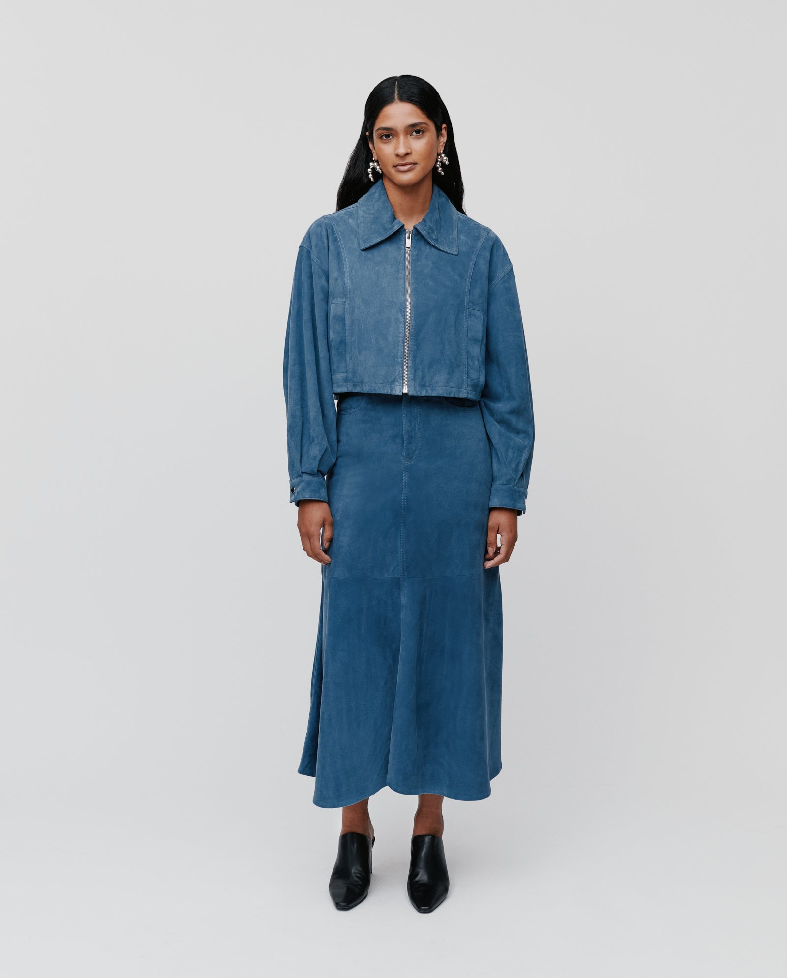 A woman in an IVY OAK blue zip-up jacket and matching high-waist LACY Skirt stands against a plain light background.