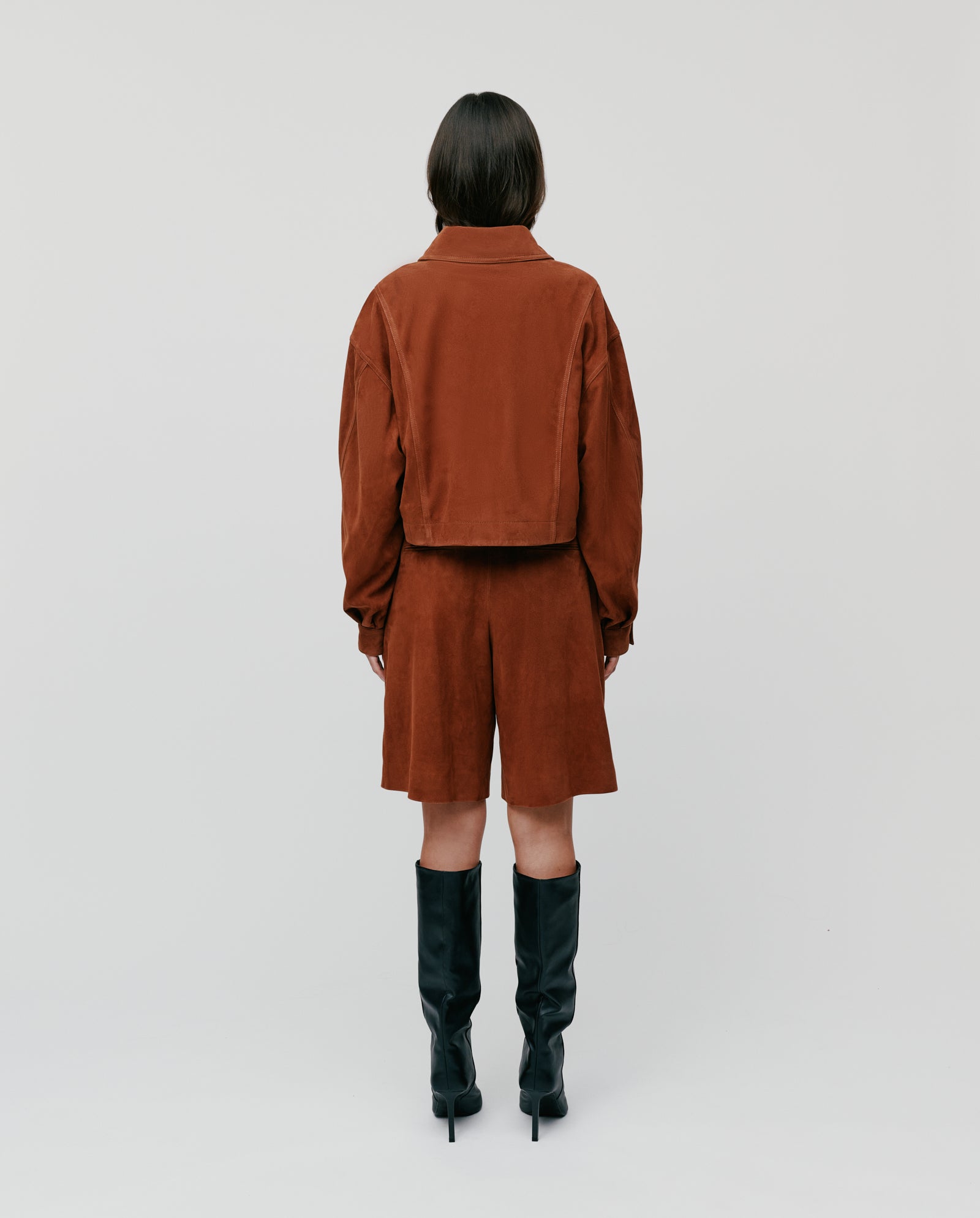 Model in the IVY OAK LENA Jacket paired with shorts and black knee-high boots, standing with back to camera against a plain background.