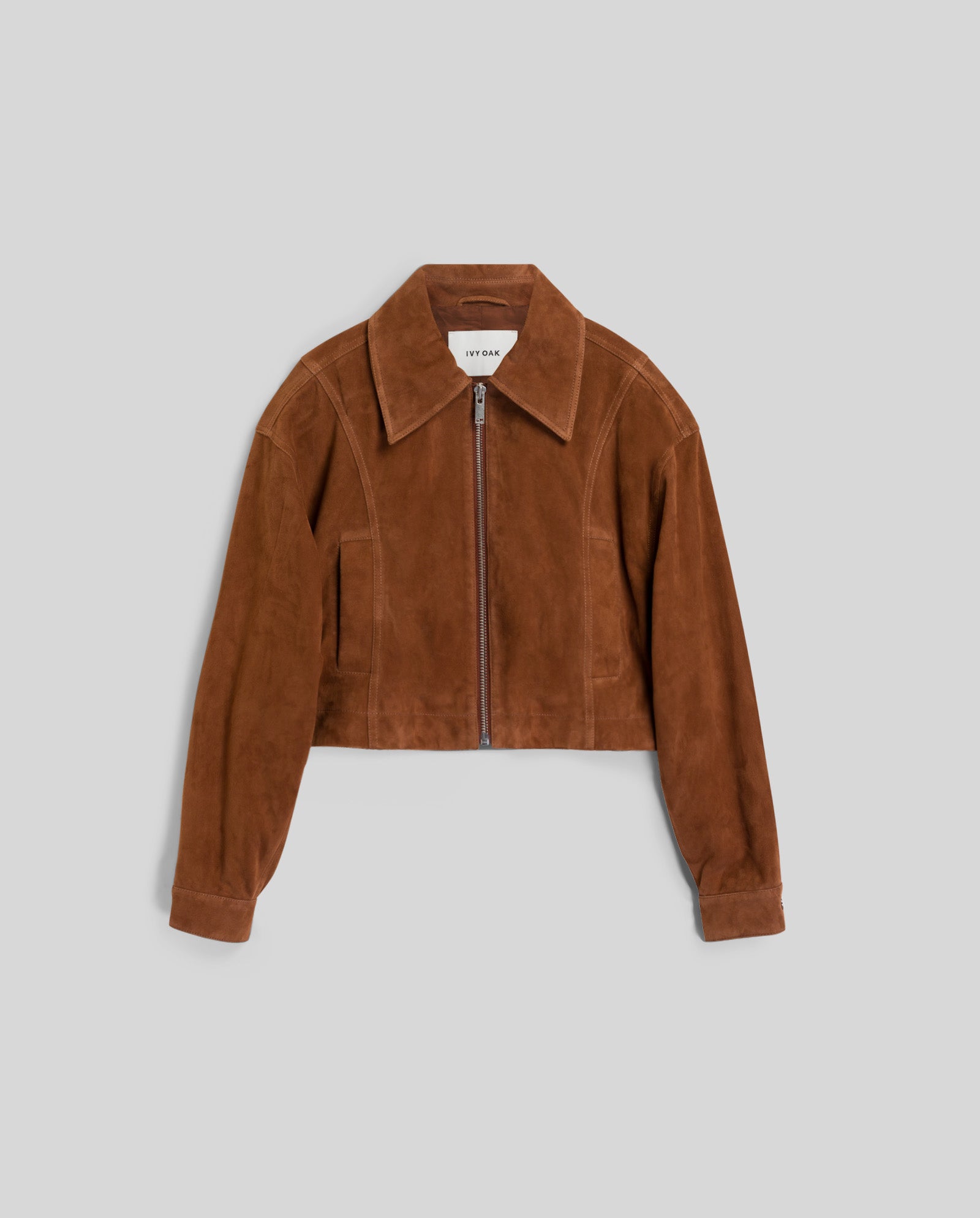The LENA Jacket by IVY OAK is a brown suede bomber with a cropped, boxy fit, front zipper, wide collar, and long sleeves, shown on a gray background.