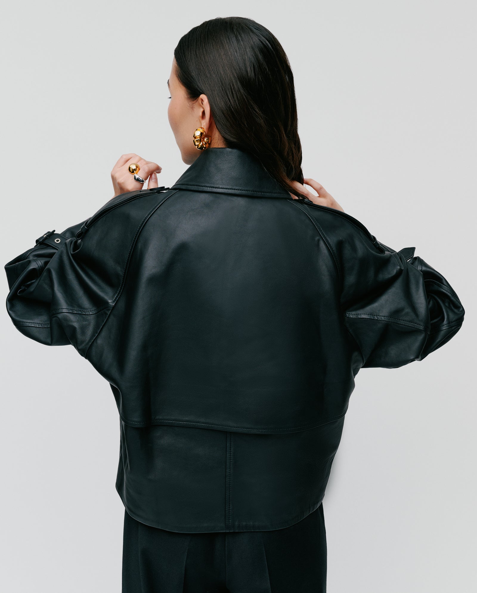 A woman with long dark hair, seen from the back, wears the oversized LUNA Jacket by IVY OAK and gold earrings.