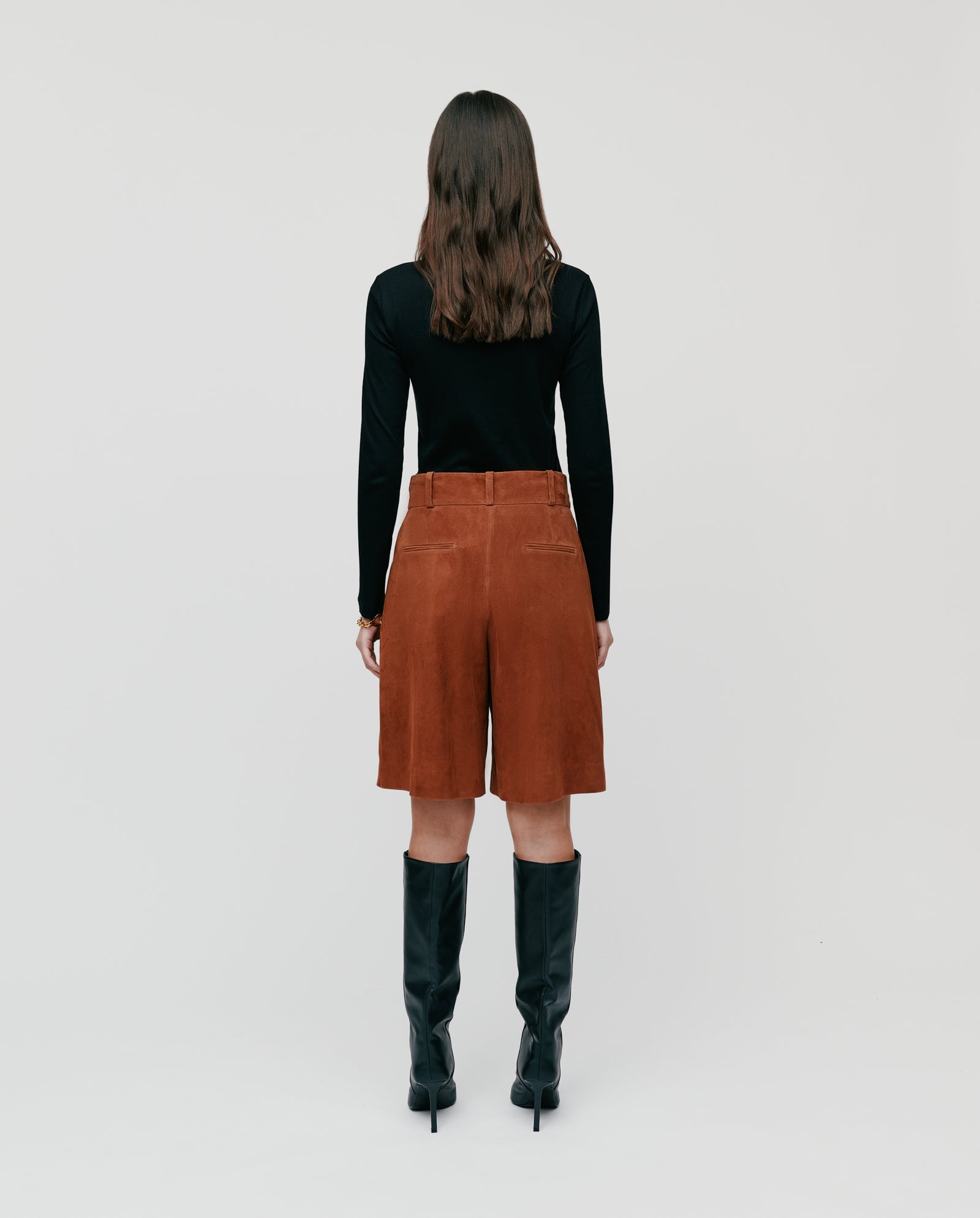 Woman with long brown hair, wearing a black top and IVY OAK LEA Trousers, paired with tall black leather boots, facing away.