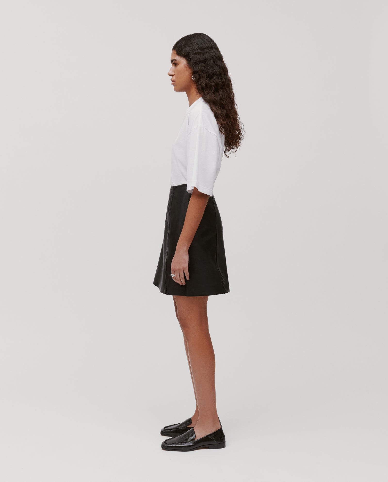 A woman stands in profile against a plain background wearing the IVY OAK LIANA SUE Skirt, a white t-shirt, and black shoes.