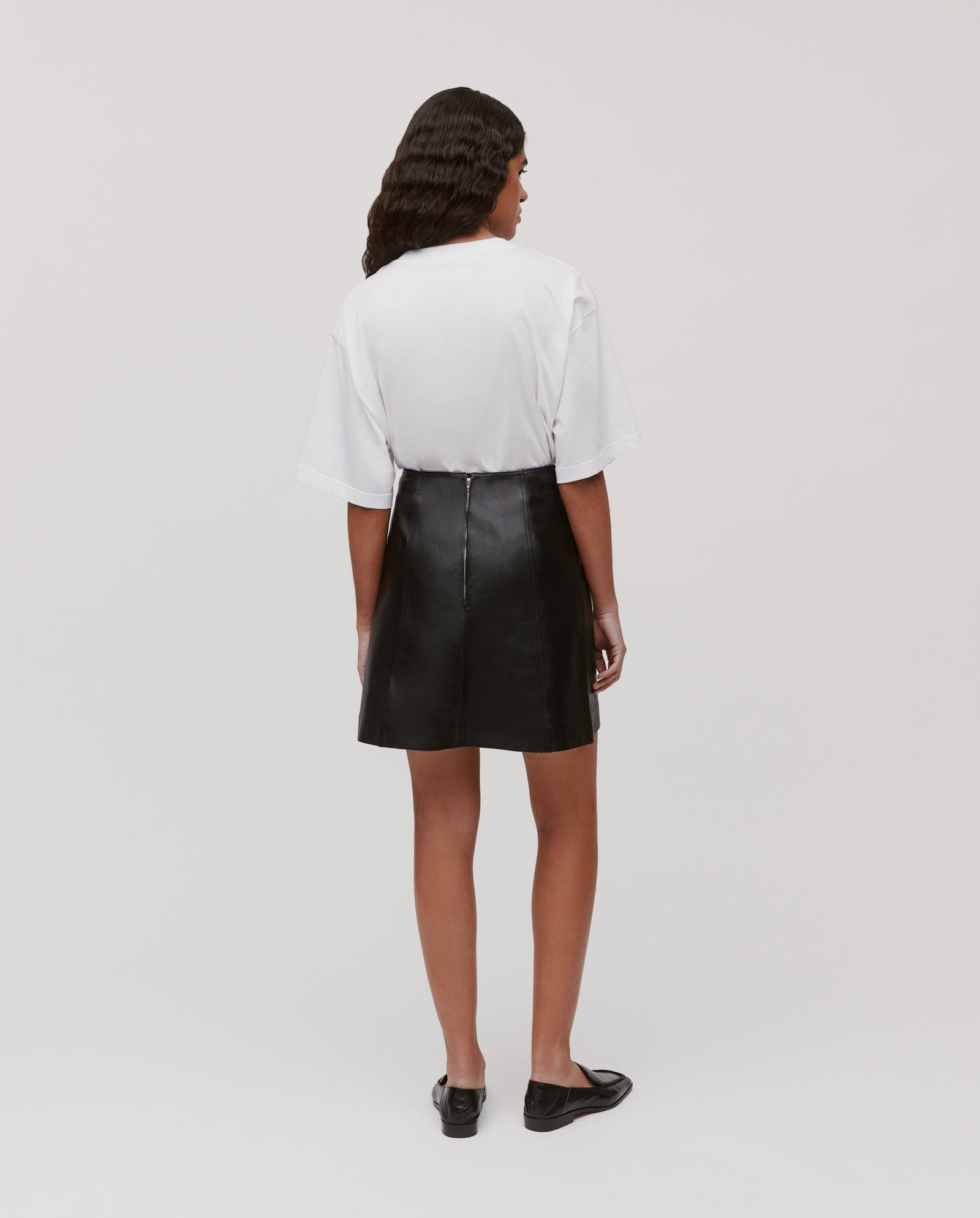 A woman faces away against a plain background, wearing the IVY OAK LIANA SUE Skirt paired with a white T-shirt and black shoes.