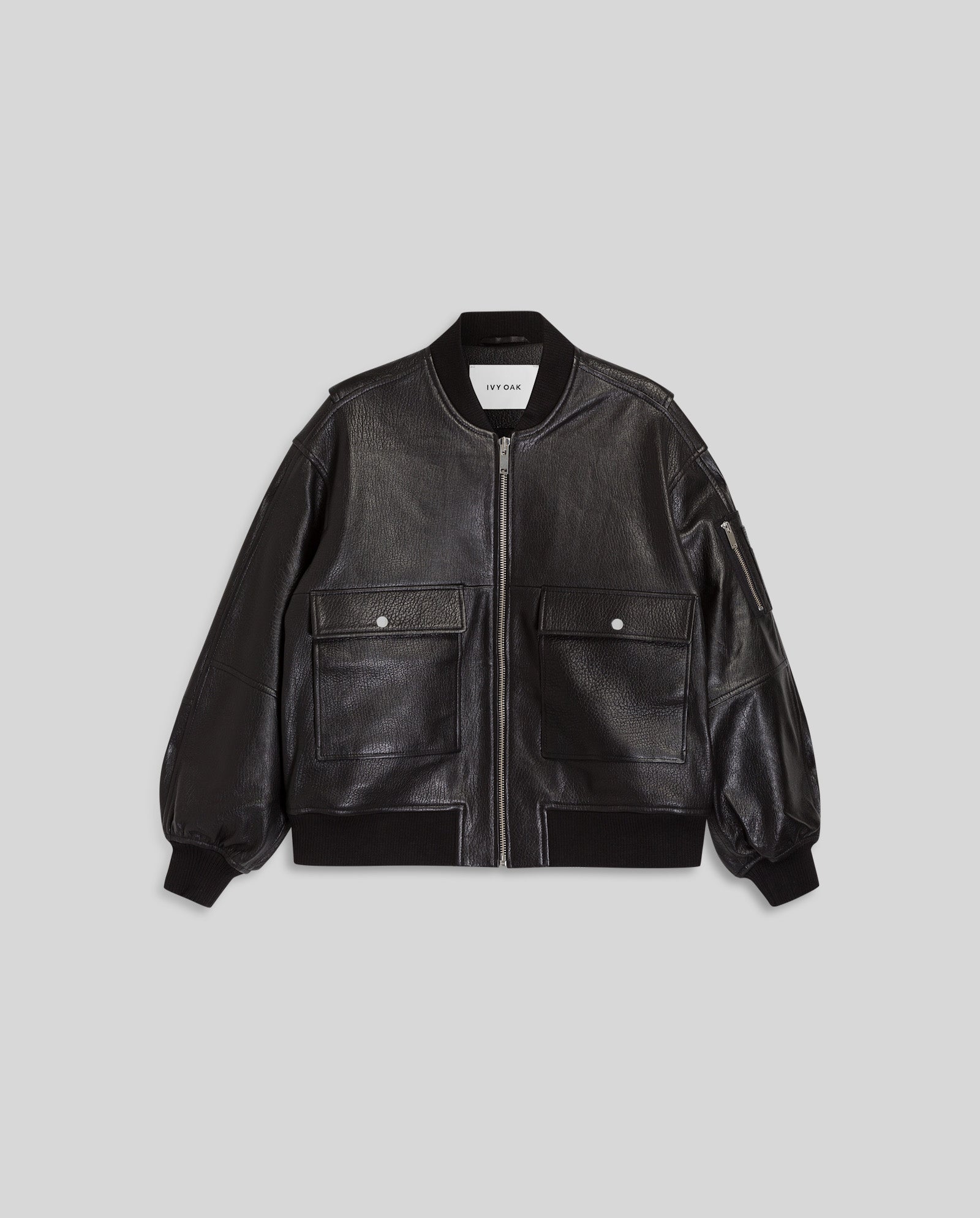 The LARA Jacket by IVY OAK is an oversized black leather bomber featuring a front zipper, two large pockets, ribbed cuffs and hem, and a patched sleeve pocket. Made from premium hide for lasting durability and comfort.
