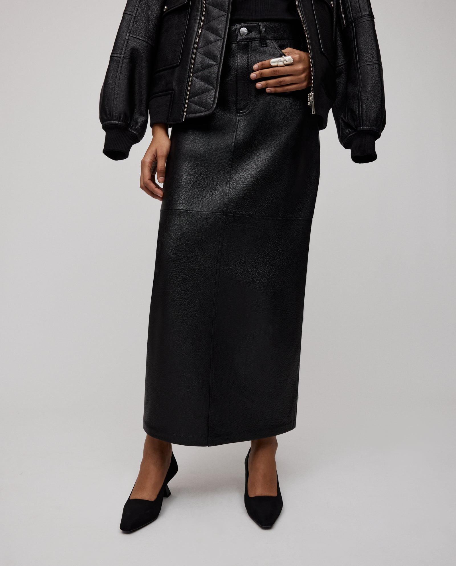 Model styled in the IVY OAK LISANNE Skirt, featuring premium hide and an A-line, ankle-length silhouette, paired with a black jacket and heels; shown from shoulders down.