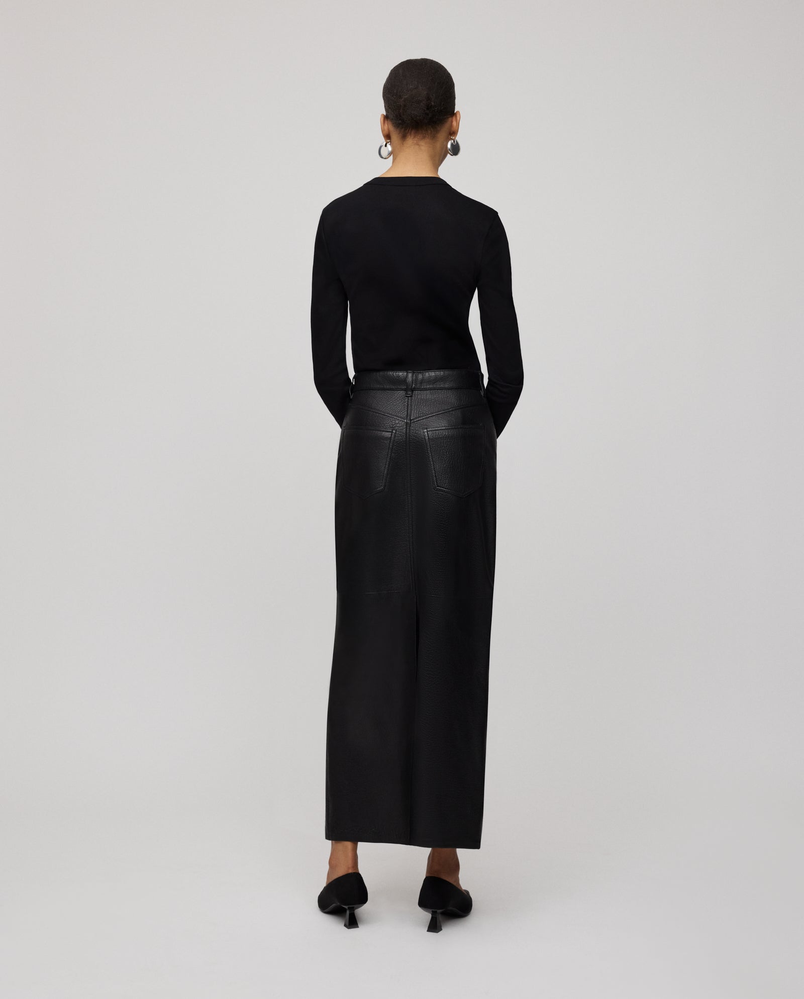 Person facing away from the camera, dressed in a black top, black shoes, and the IVY OAK LISANNE Skirt—an ankle-length design with a sleek A-line silhouette.