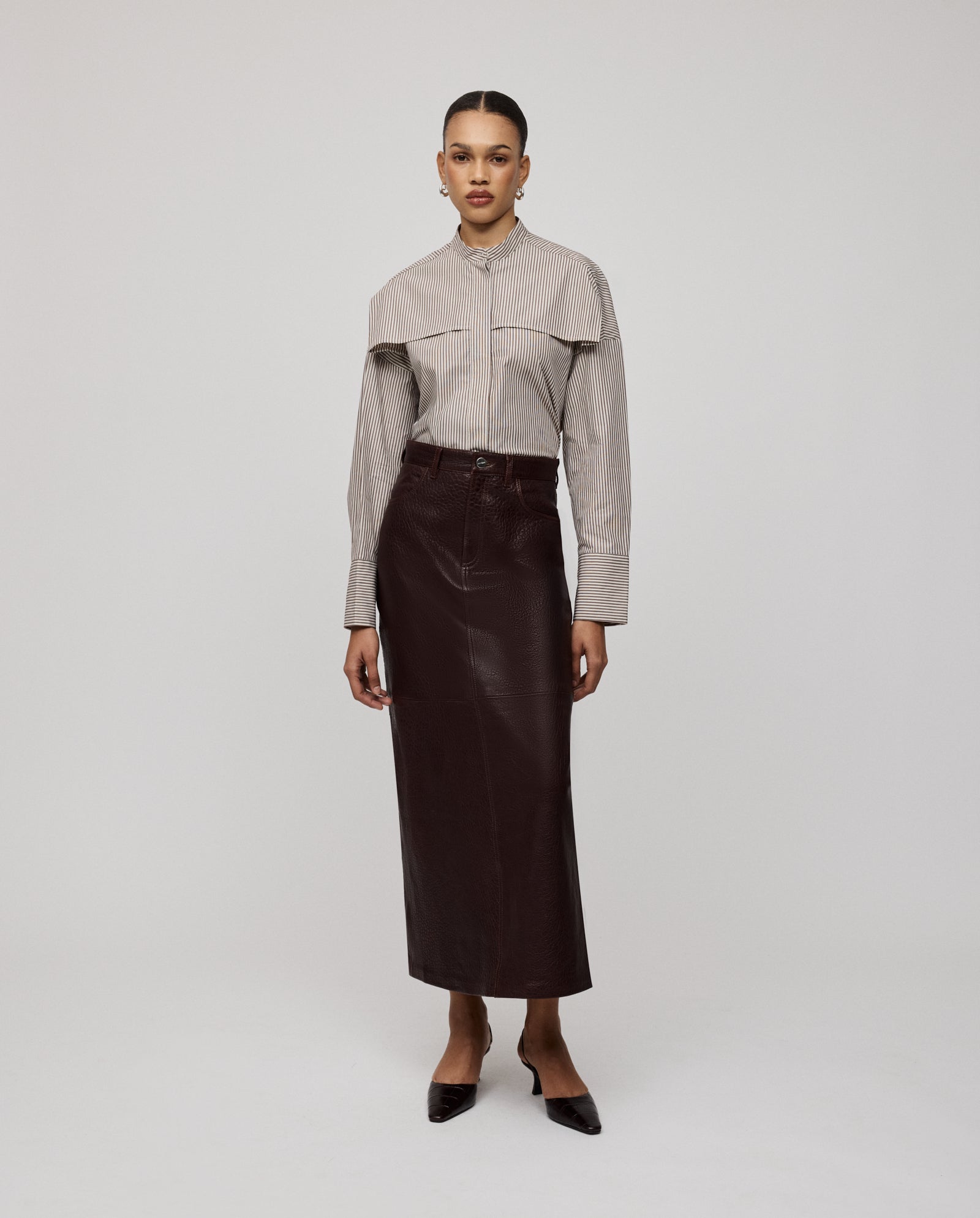 A woman in a striped shirt, heels, and the IVY OAK LISANNE Skirt with an ankle-length A-line silhouette stands against a plain light background.