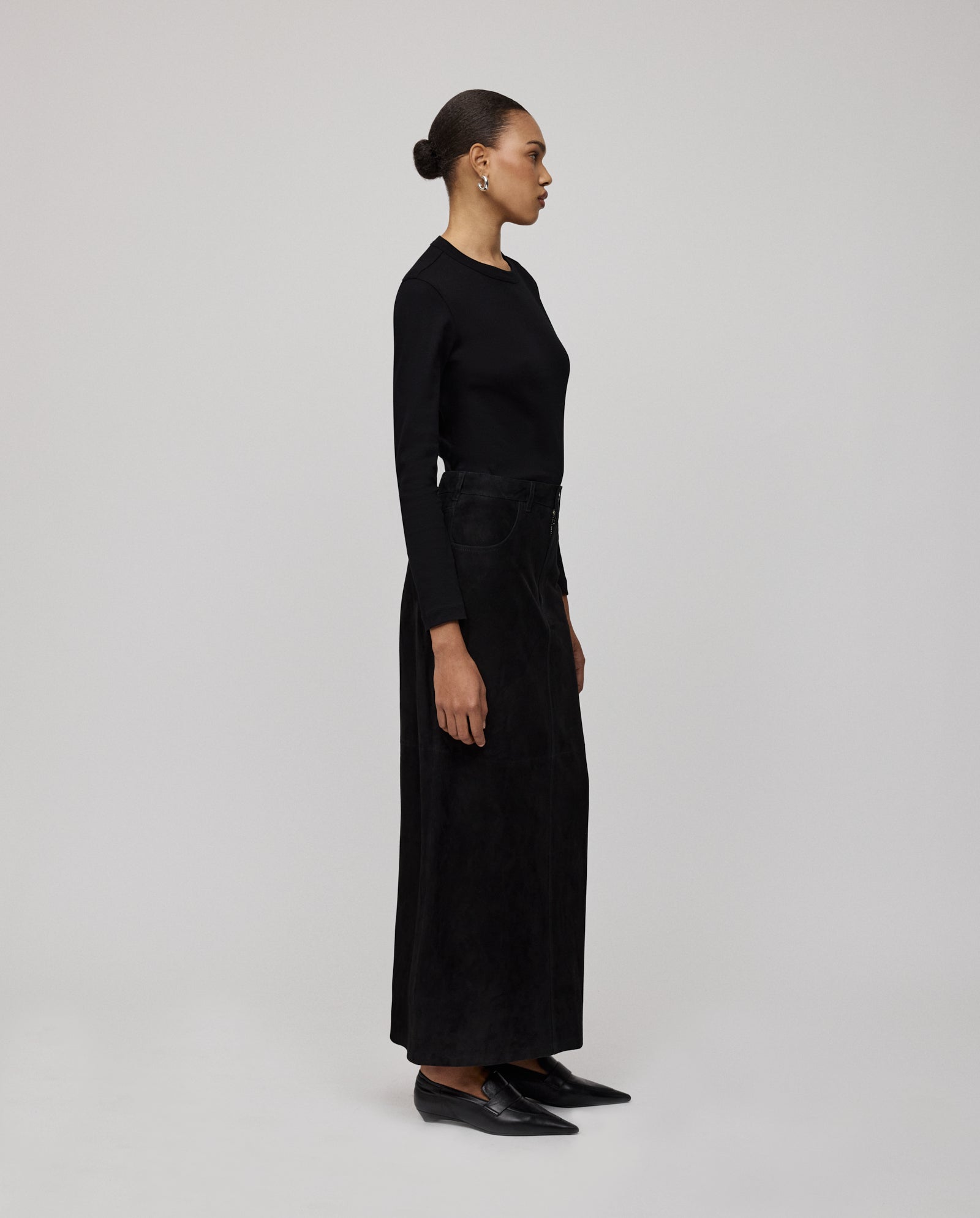 A woman wearing the IVY OAK LISANNA ROSE Skirt, a high-waist A-line piece, pairs it with a black long-sleeve top and black shoes, standing in profile against a plain background.