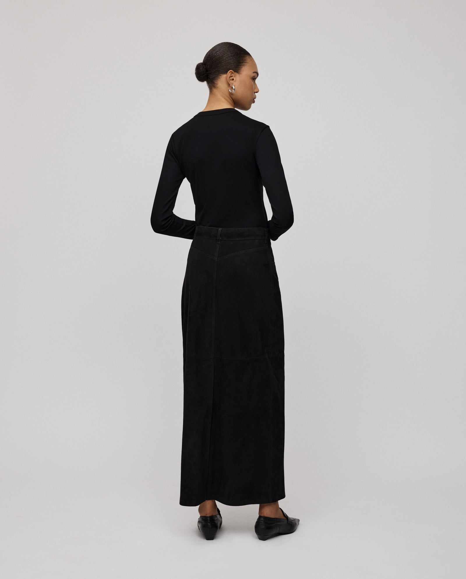 A woman stands with arms crossed, facing away, wearing the IVY OAK LISANNA ROSE Skirt and a black long-sleeve top.