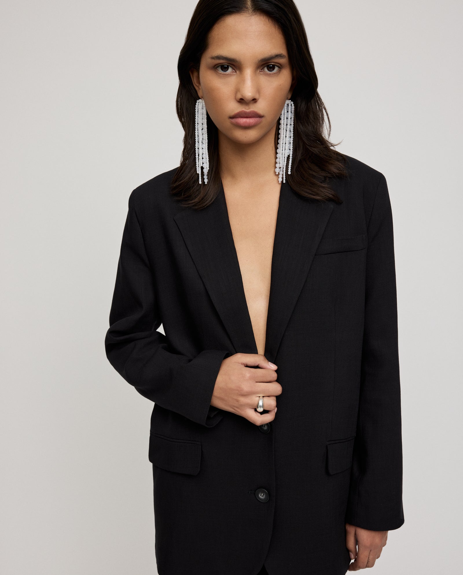 A woman wearing an oversized IVY OAK JUNA Blazer, statement earrings, and rings poses against a plain light background.