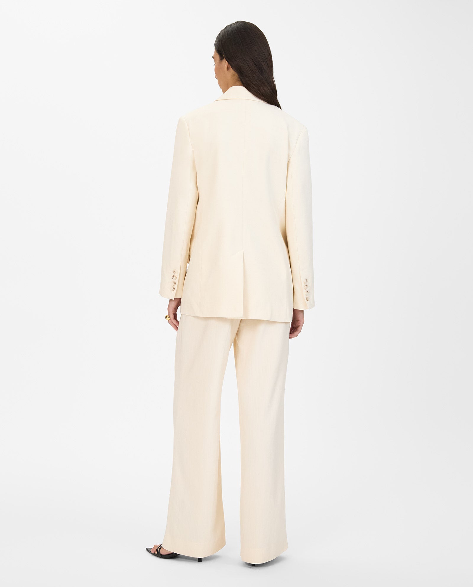 A woman with long hair faces away against a white background, wearing an oversized, cream-colored JUNA Blazer by IVY OAK, single breasted.