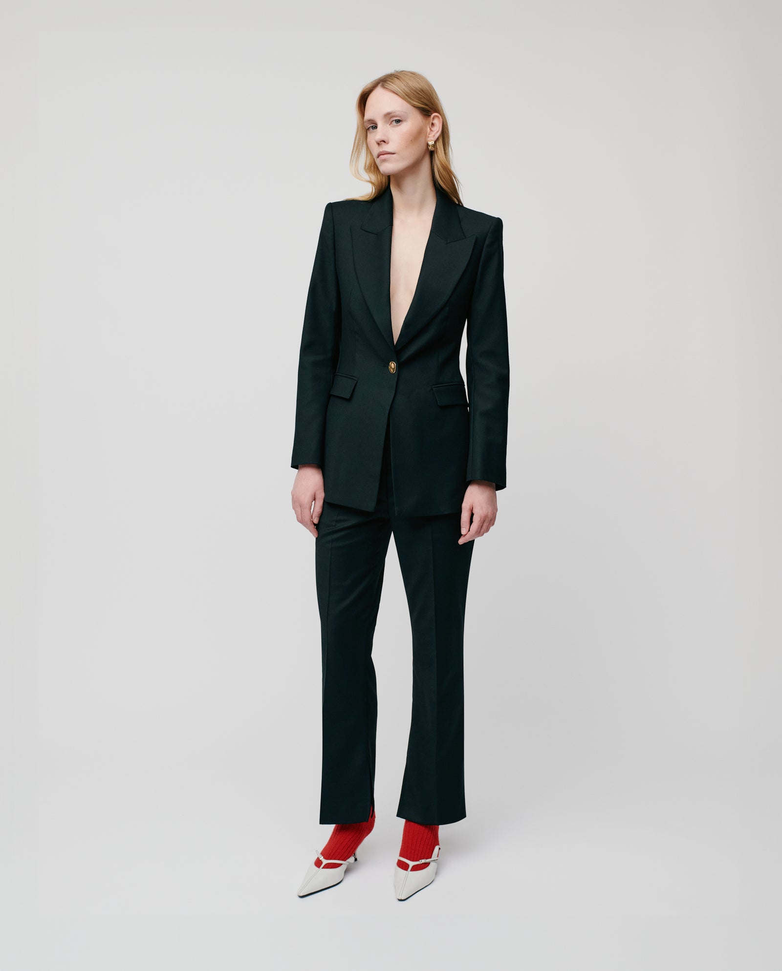 A person in an IVY OAK JOLANKA Blazer with golden buttons, black suit, red socks, and white heels stands against a plain light background.