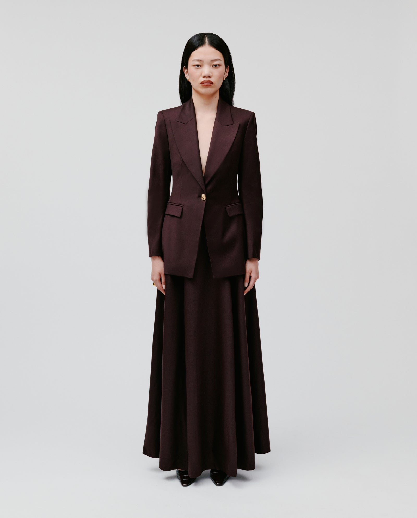A woman stands against a white background wearing the IVY OAK JOLANKA Blazer in tailored burgundy, paired with a matching long skirt.