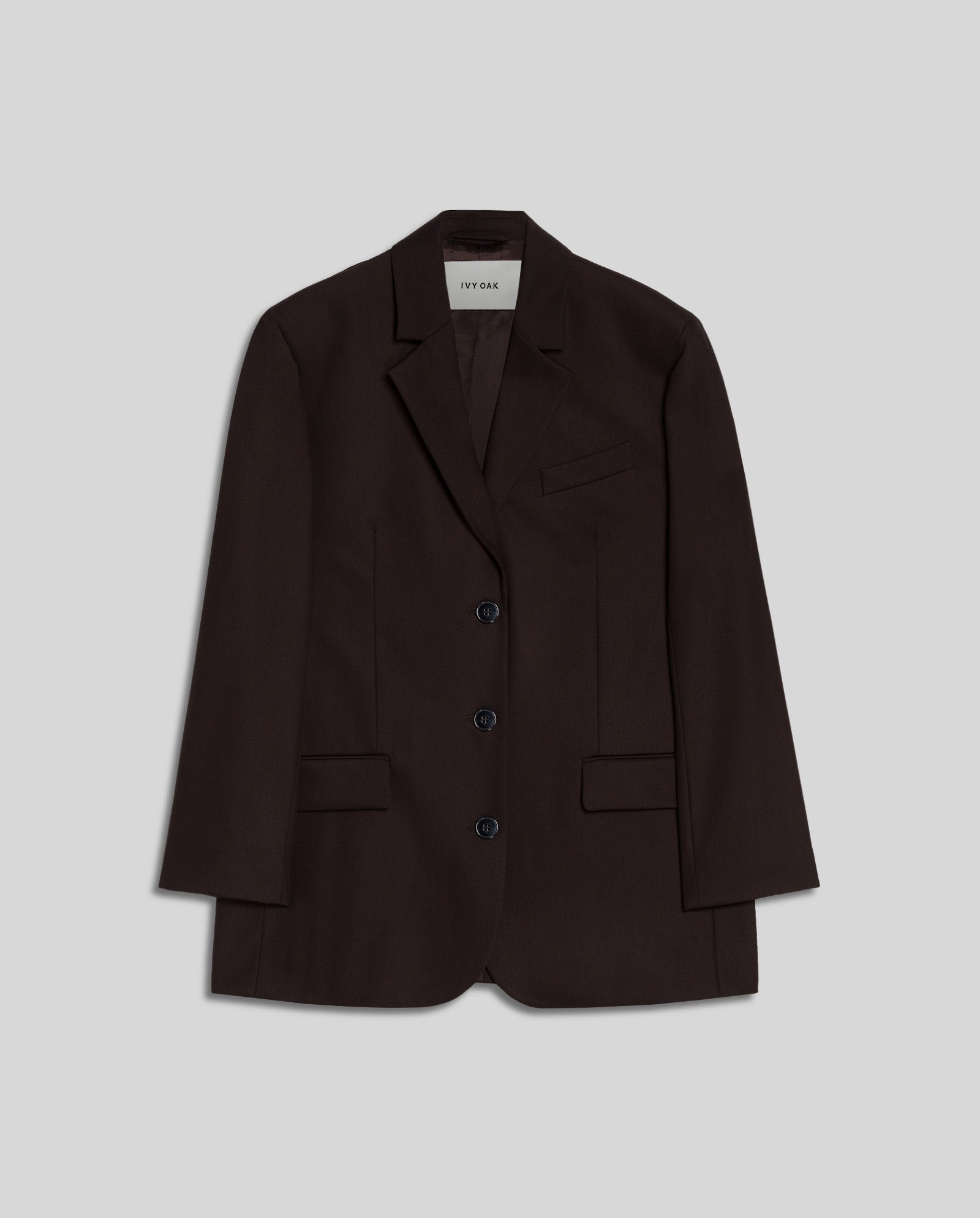 The IVY OAK JACQUELINE Blazer is a dark brown, oversized blazer featuring three front buttons, flap pockets, and a notched lapel, shown on a light gray background.