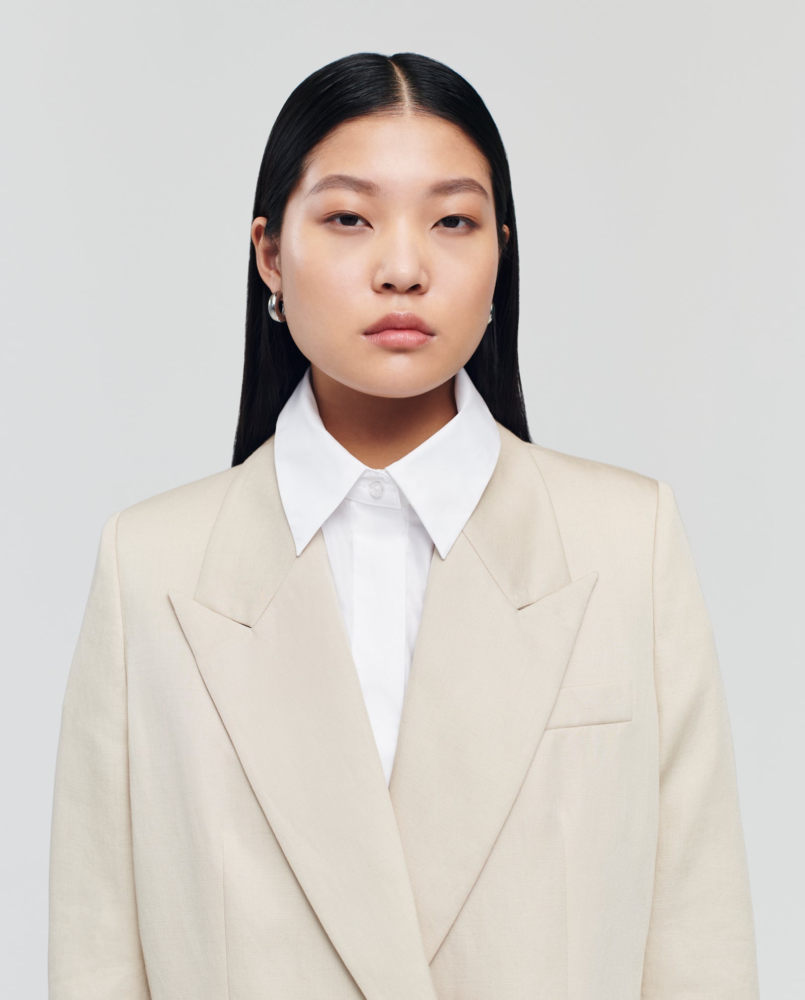 A woman with long black hair, dressed in an IVY OAK JULIETTE MARIE cream double-breasted blazer and white shirt, stands against a plain light background.