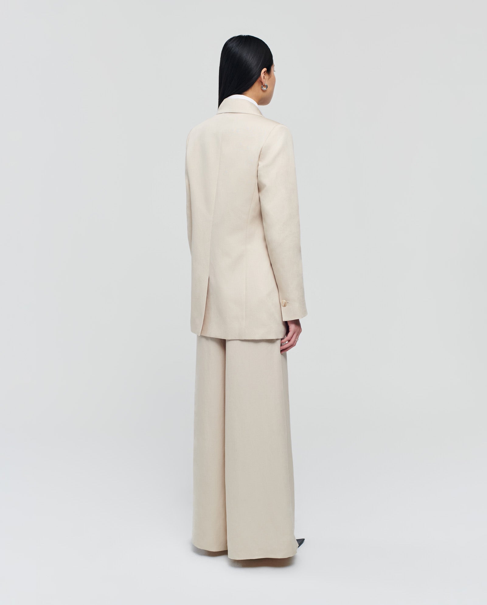 A person stands with their back to the camera, wearing the cream-colored JULIETTE MARIE Blazer by IVY OAK and matching wide-leg pants against a plain background.