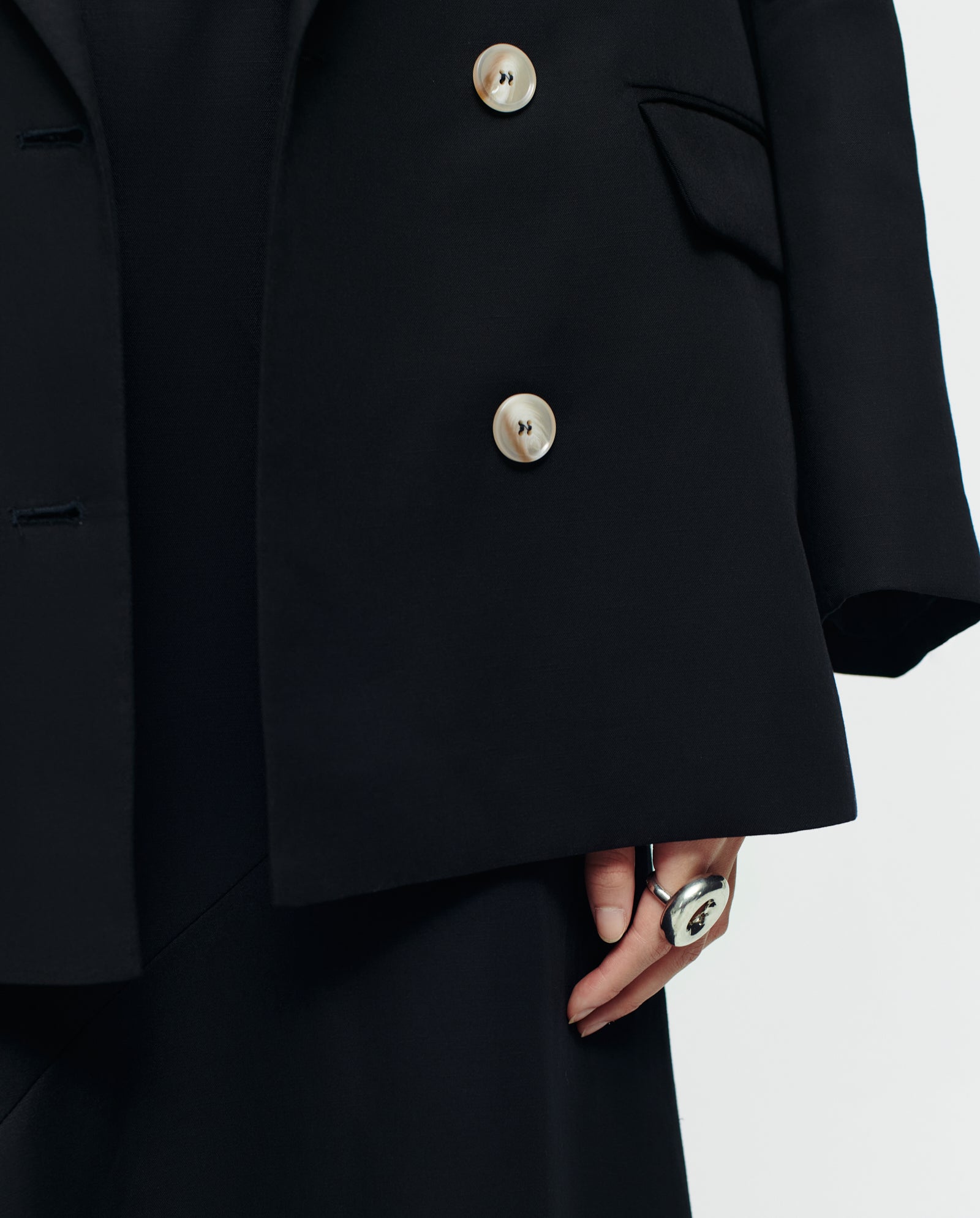 A person displays the lower half of the IVY OAK JULIETTE MARIE double-breasted linen-blend blazer in black with gold buttons, wearing a ring and showing only their hand.