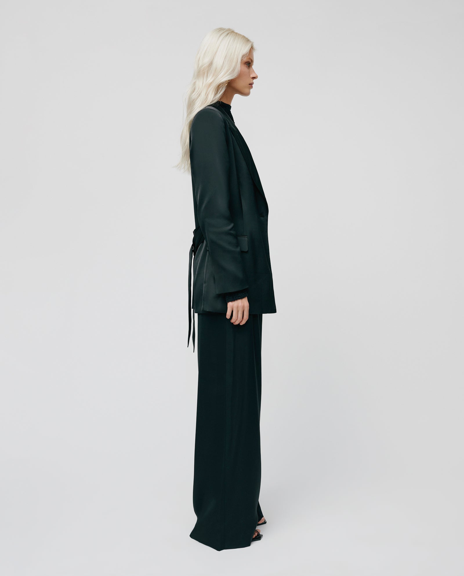 Woman with long blonde hair wears an IVY OAK JOSEPHINA Blazer and PRIYA ANN trousers, standing in profile against a plain light background.