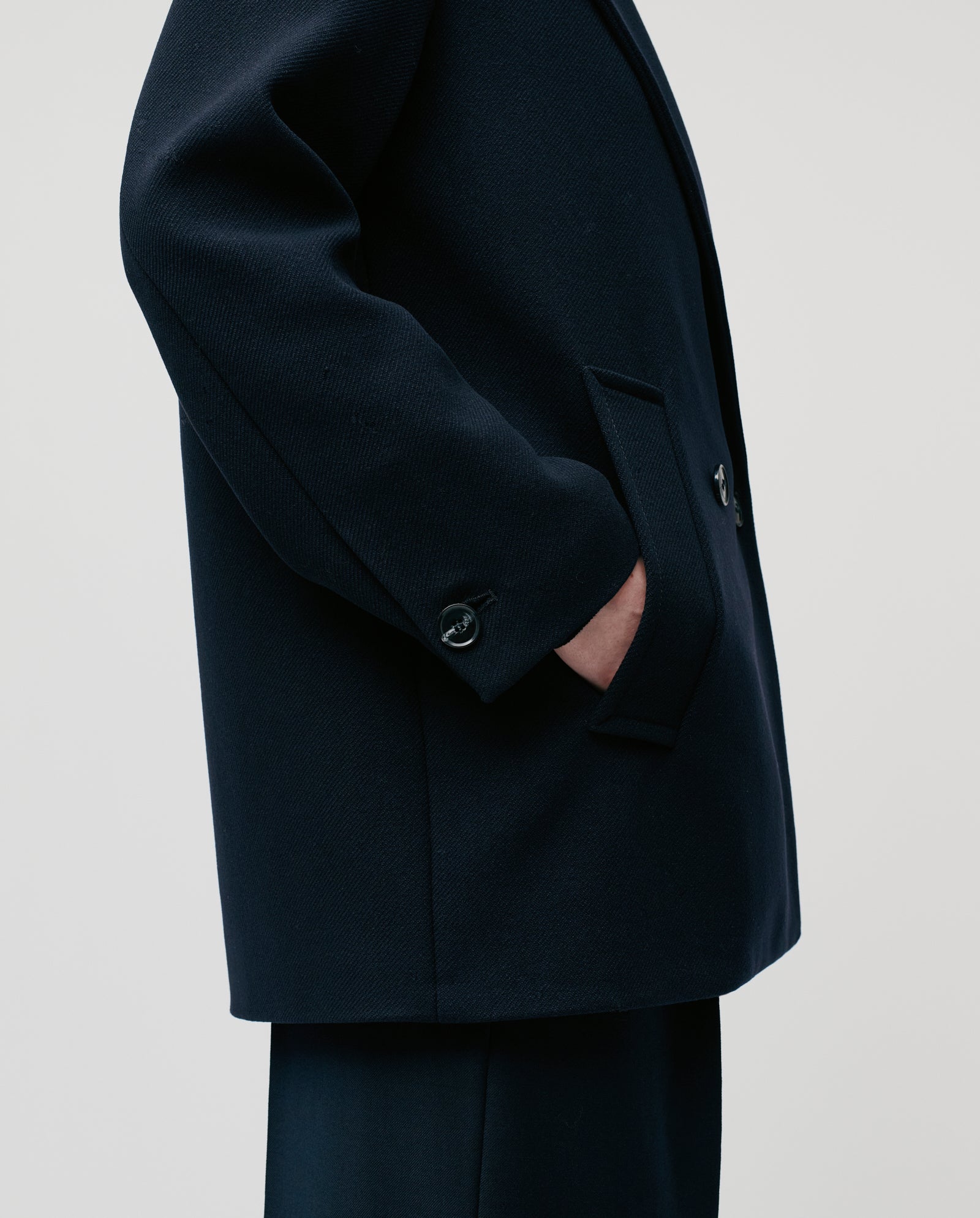 A person wearing the IVY OAK JENNA double-breasted, oversized winter jacket stands in profile with one hand in a pocket against a plain background.