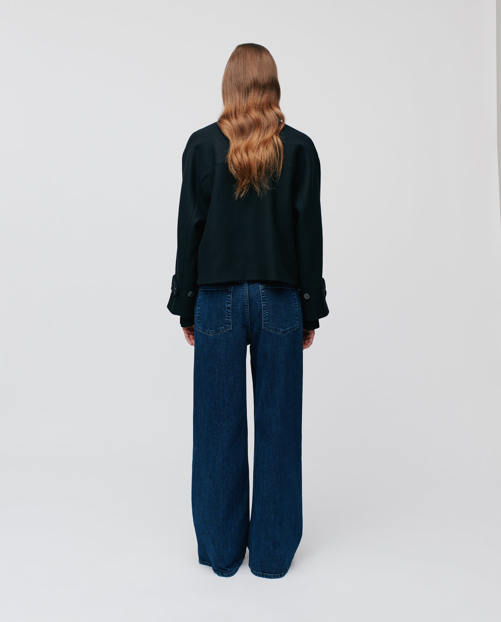 A person with long wavy hair, seen from behind, wears the IVY OAK JANET Jacket in black cashmere blend and wide-leg jeans.