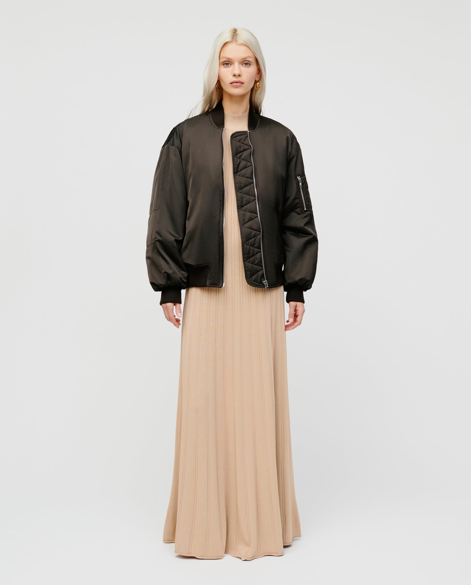 A woman wears the IVY OAK JANE Jacket—an oversized bomber with a metal zipper—over a long beige dress, standing against a plain white background.