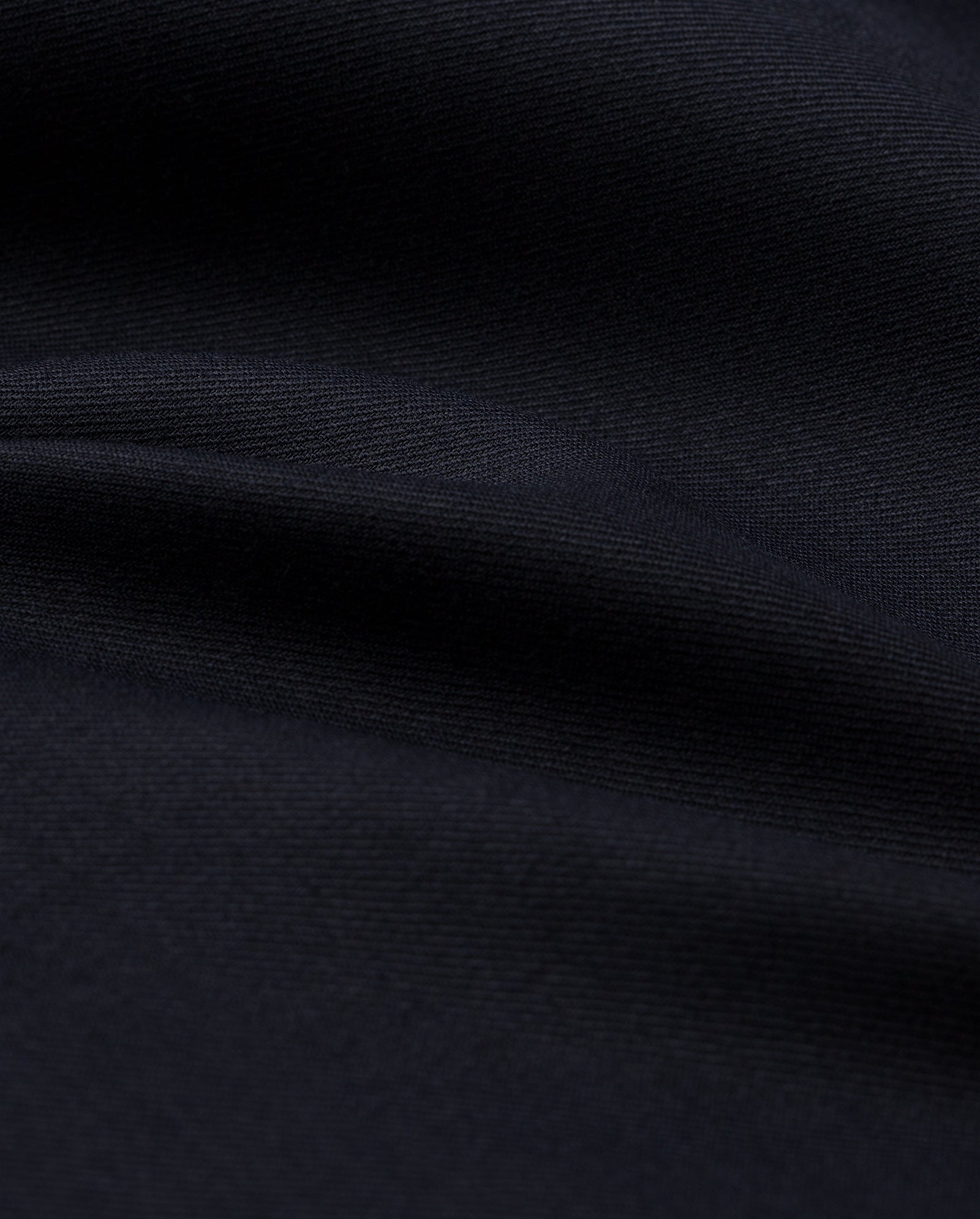 Close-up of smooth, dark fabric with gentle folds and soft shadows, evoking the refined texture of IVY OAKs PRESCILLIA Trousers.