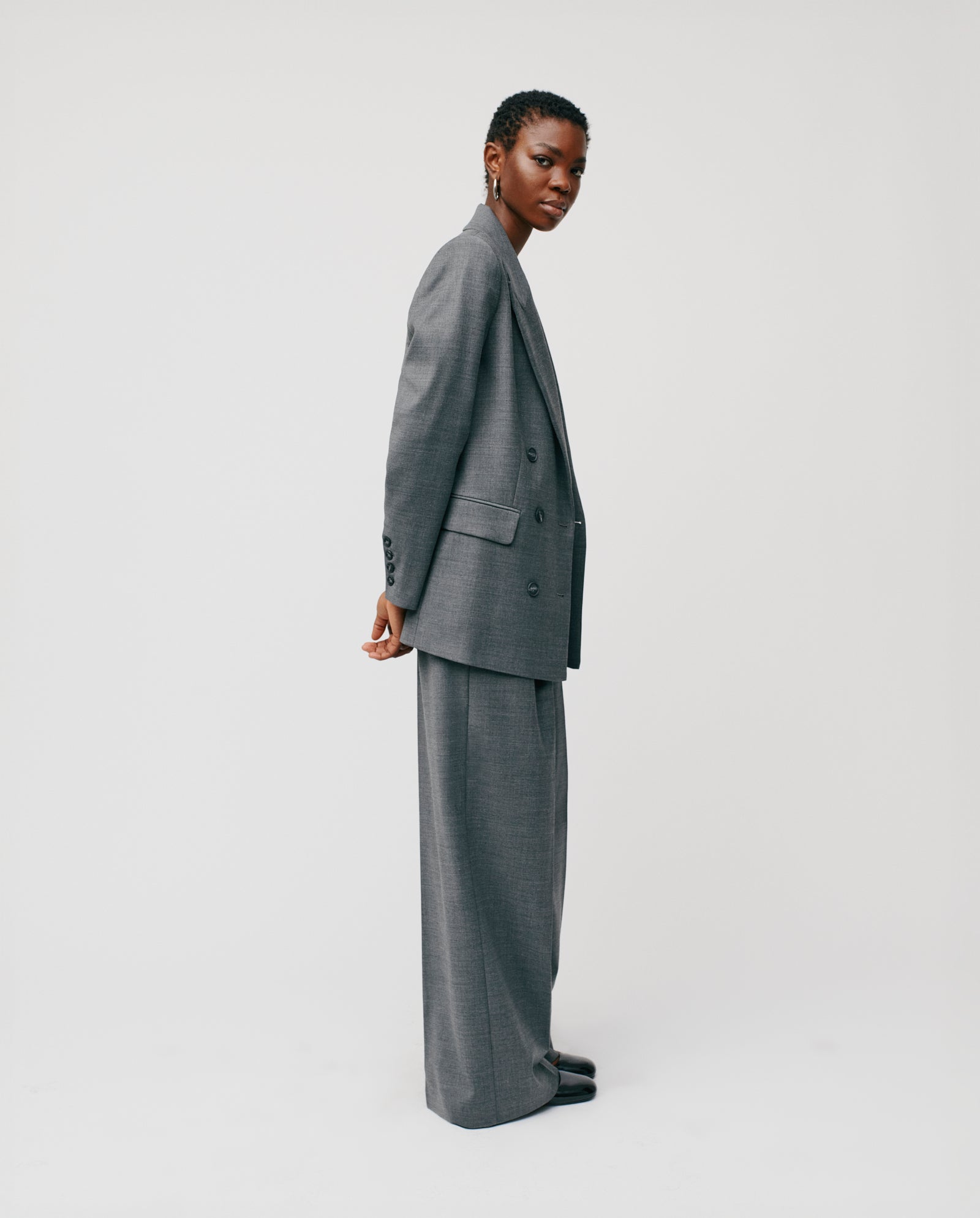 Model wears the IVY OAK JULIETTE ROSE Blazer, a loose-fitting gray double-breasted style, paired with black shoes, standing against a plain white background and looking at the camera.