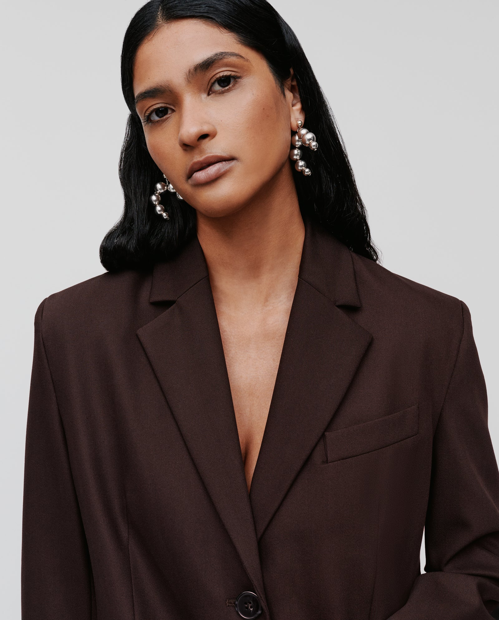 A woman wearing the IVY OAK JACQUELINE Blazer and pearl earrings gazes at the camera with a neutral expression.