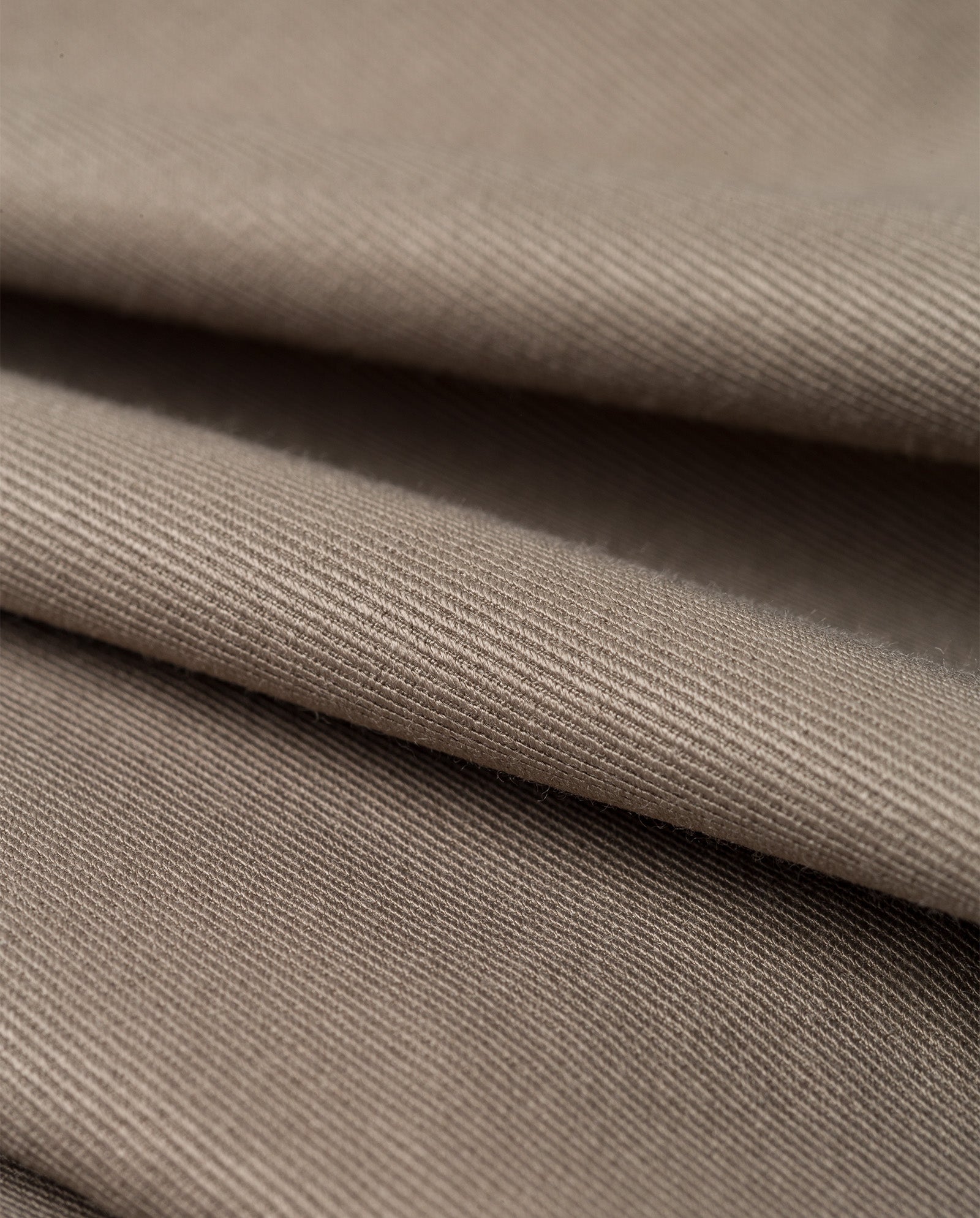 Close-up of folded khaki fabric reveals its smooth texture and fine diagonal weave, perfect for crafting the IVY OAK JACQUELINE Blazer in an oversized, boxy fit.