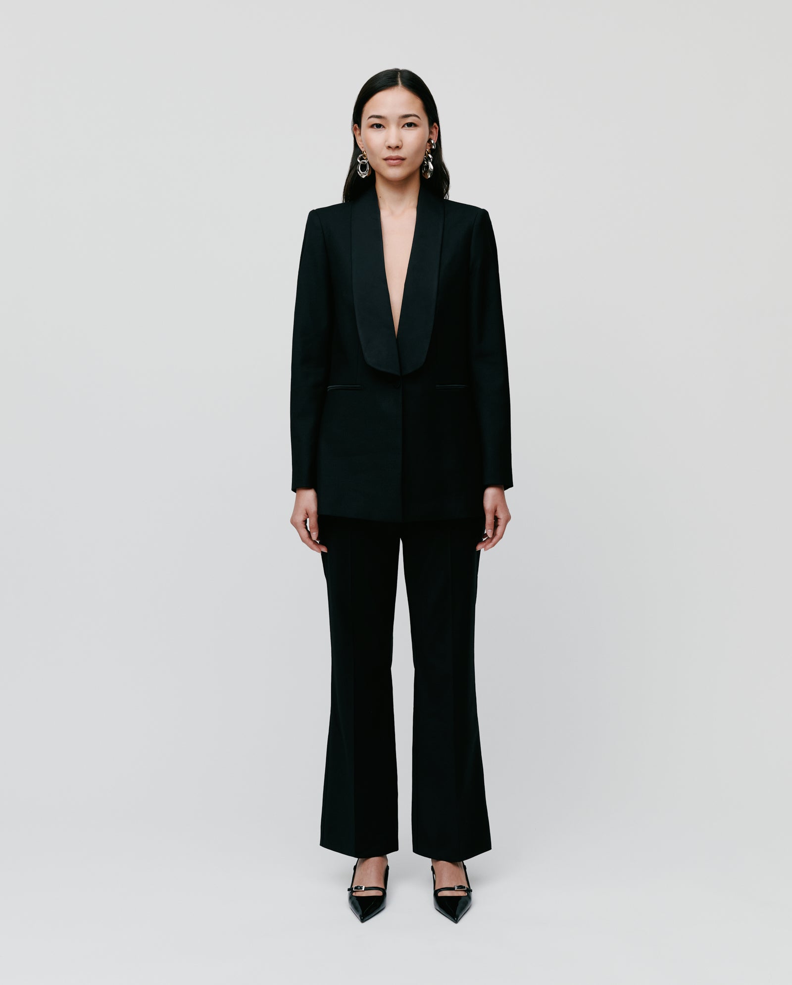 A woman wearing the IVY OAK JANA MIA black regular fit shawl collar blazer with front button closure and heels stands facing forward against a plain white background.