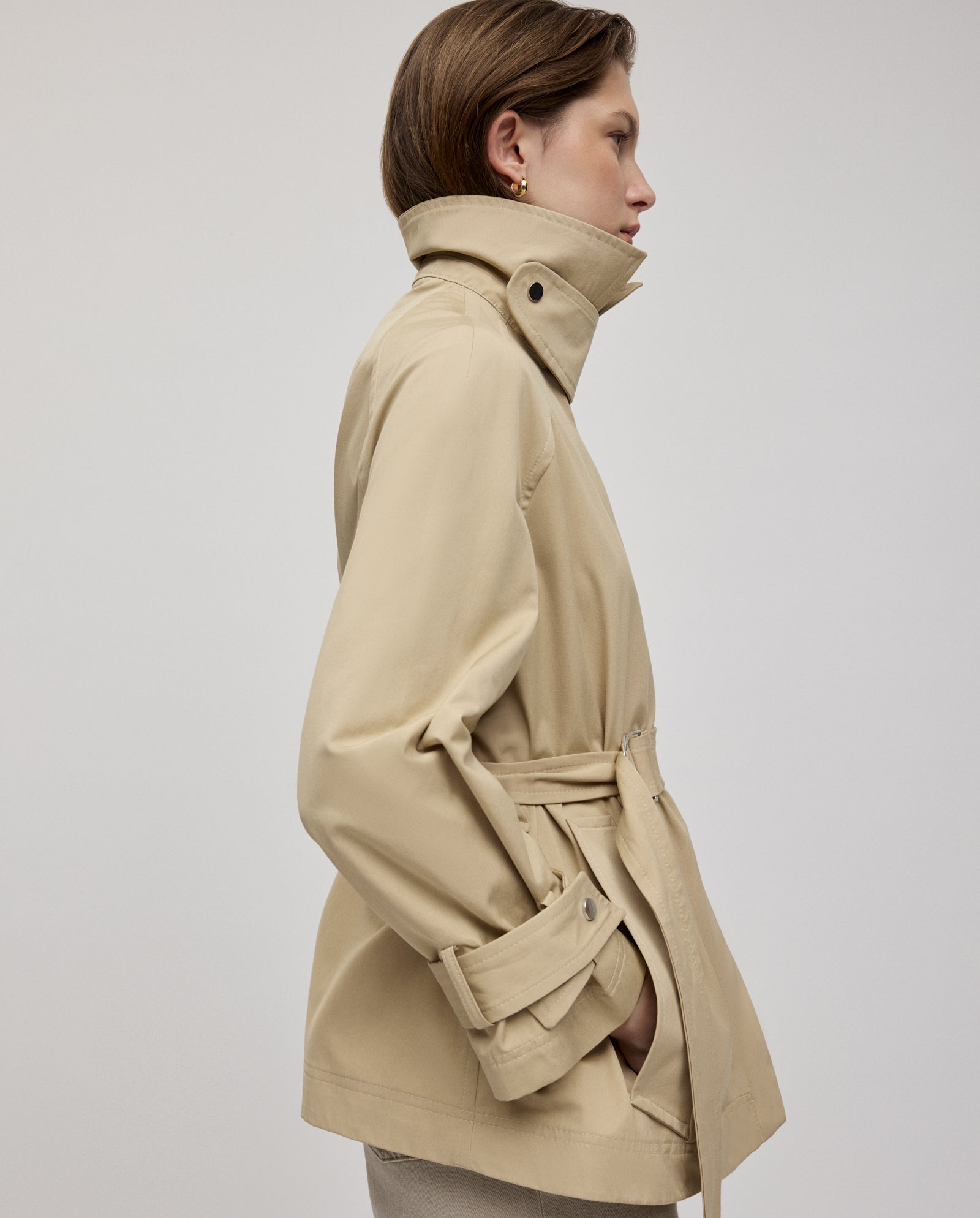 A woman in profile wears the IVY OAK JULES Jacket, a beige A-line trench, set against a plain light background.