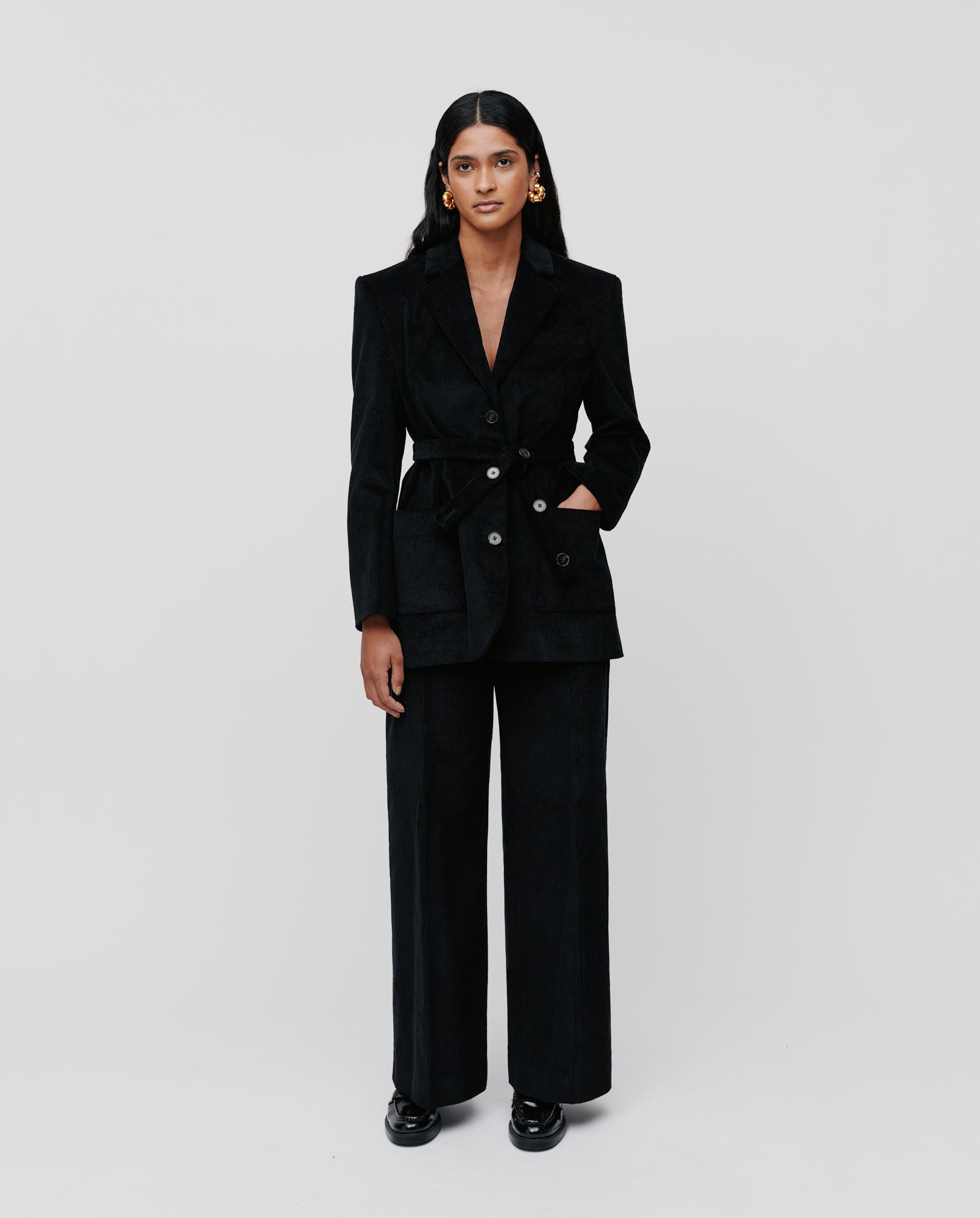 A woman stands against a plain white background wearing the IVY OAK JACQUELINE BEA oversized corduroy blazer with a removable belt and wide-leg pants.