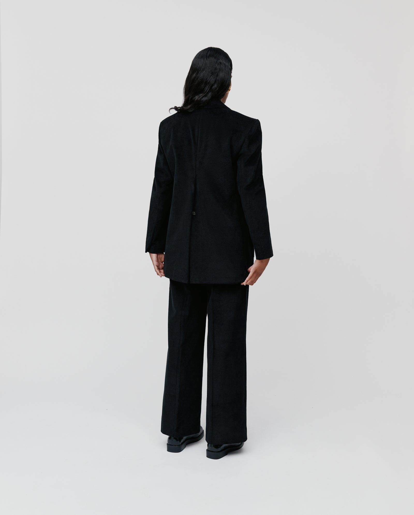 Person facing away against a plain background, wearing the IVY OAK JACQUELINE BEA Blazer—an oversized corduroy piece with a long back vent—paired with black wide-leg pants.
