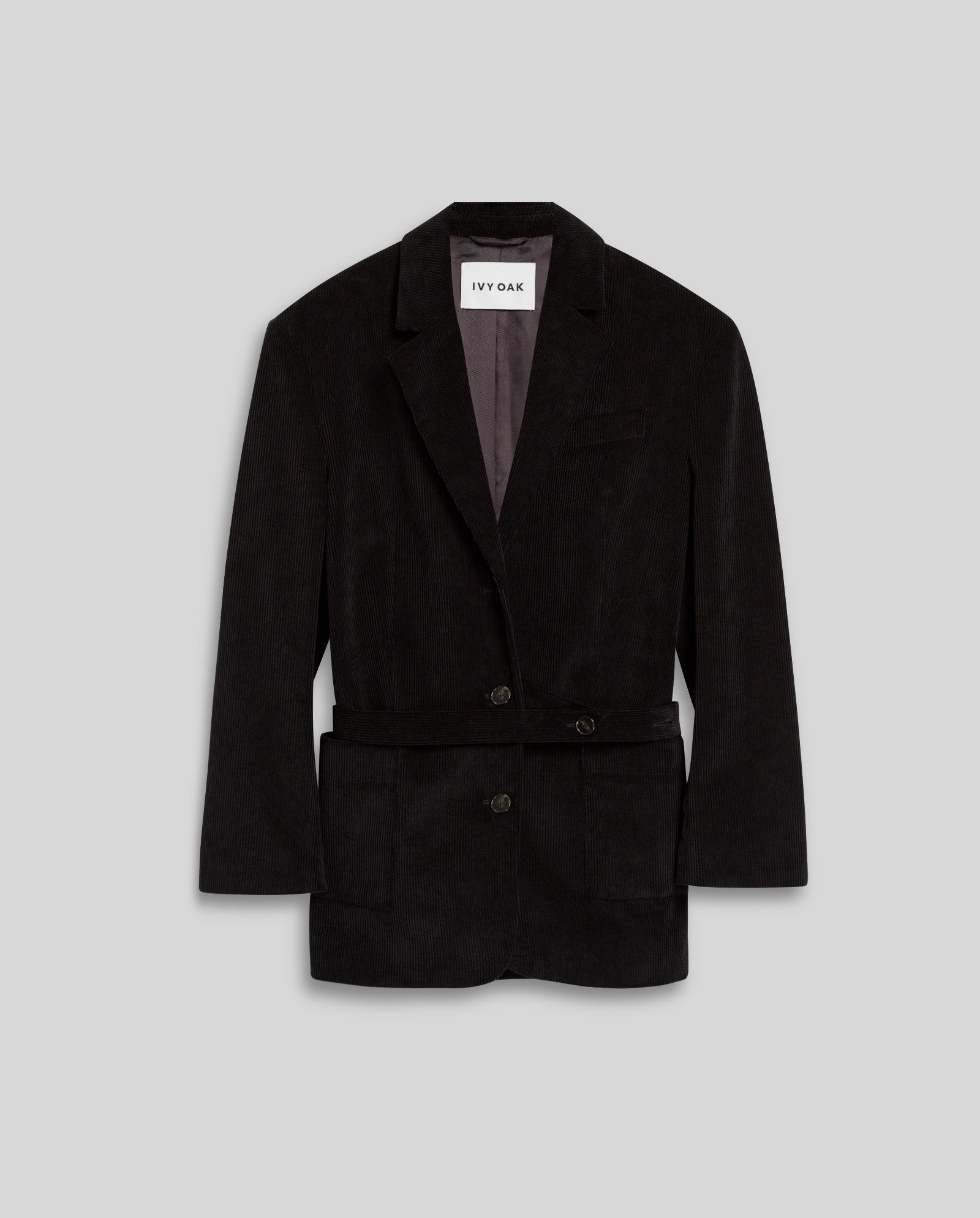The IVY OAK JACQUELINE BEA Blazer is a black oversized corduroy piece with a notch lapel, two buttons, front pockets, and a long back vent, shown against a gray background.