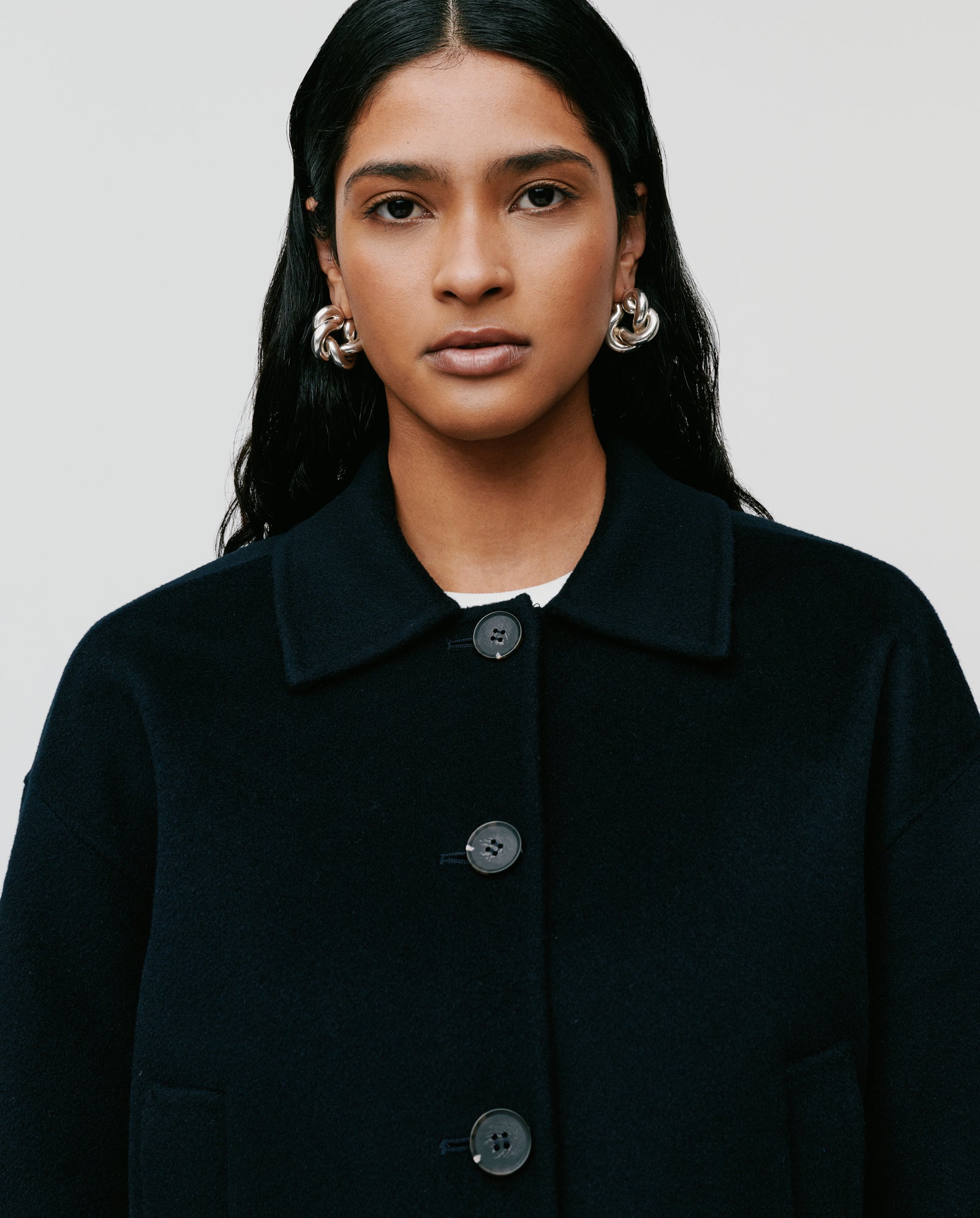 Woman with long dark hair faces forward wearing the IVY OAK JAIA Wooljacket, made from luxurious double-faced fabric and responsible wool, paired with large silver hoop earrings.