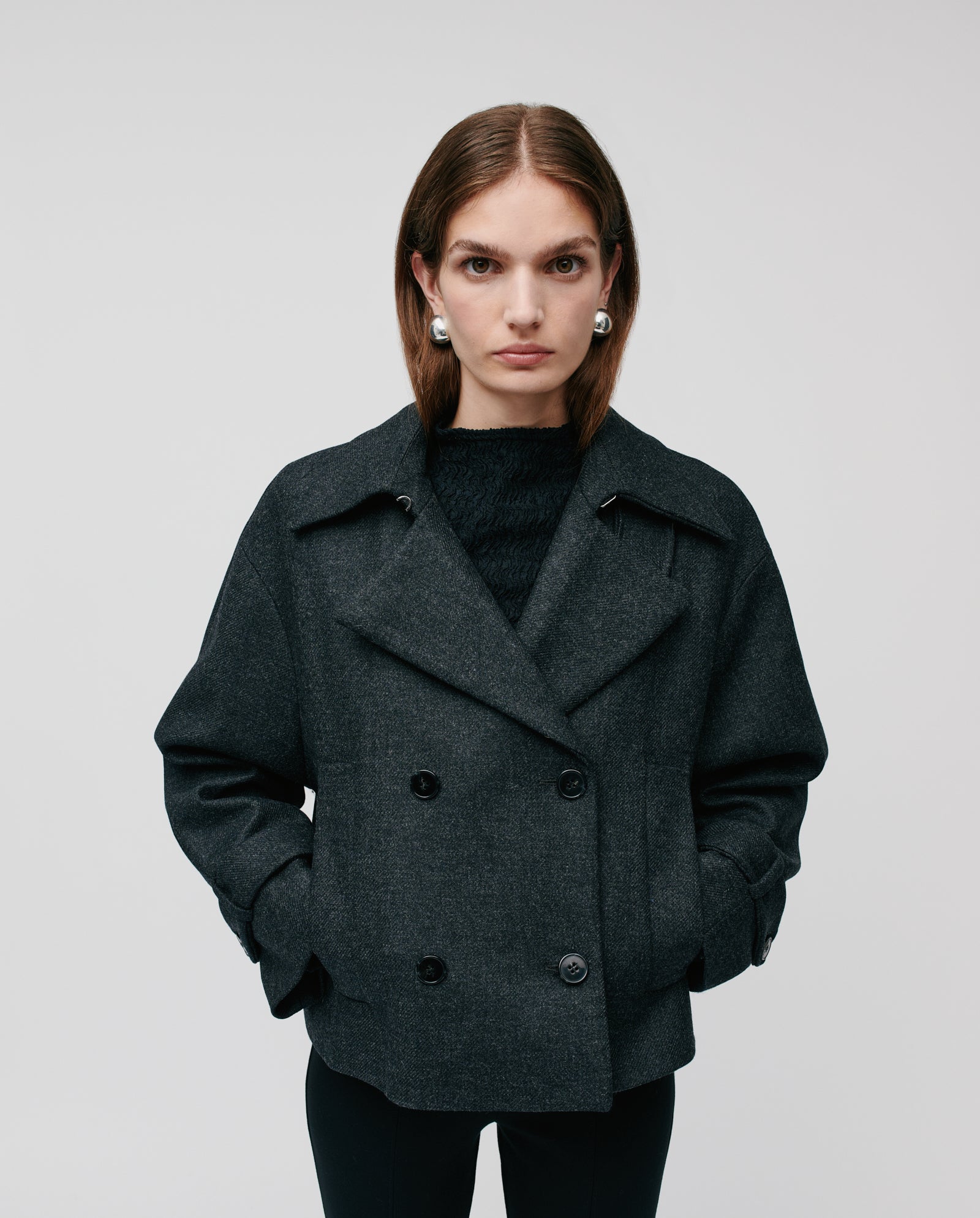A woman wears the IVY OAK JANET Wool Blazer in a double-breasted Trench-Look style with hands in pockets and silver earrings, standing against a plain background.