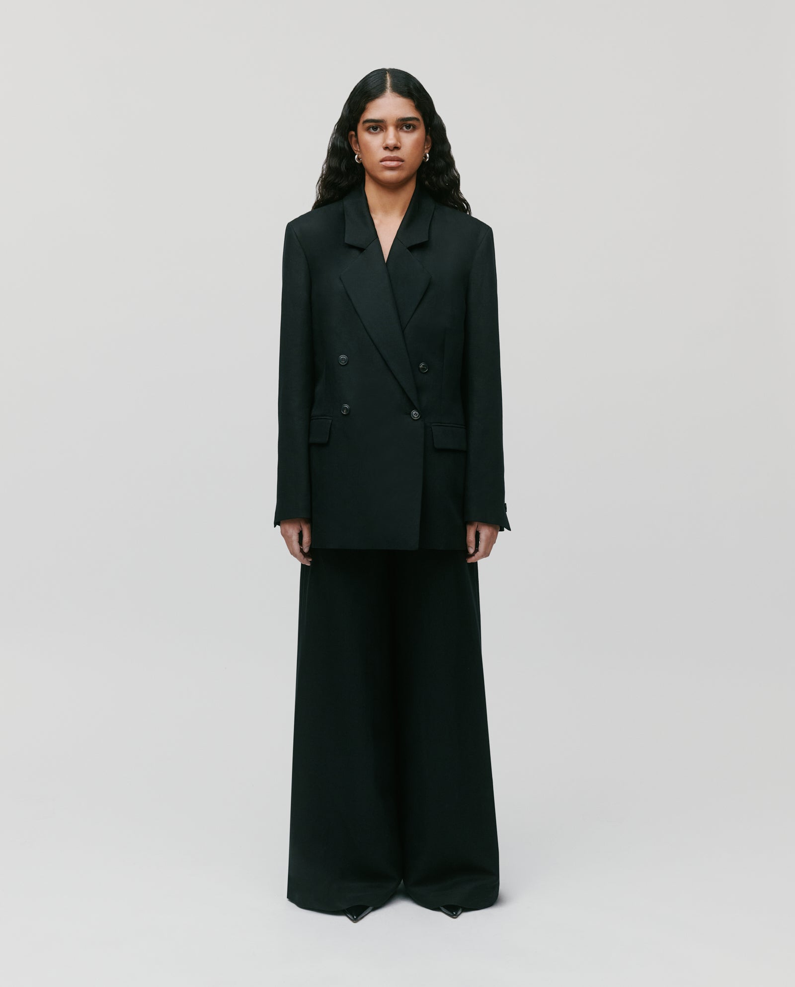 A person wears the IVY OAK JASEMINA ROSE Blazer, a black oversized linen piece, paired with wide-leg pants, set against a plain light background.