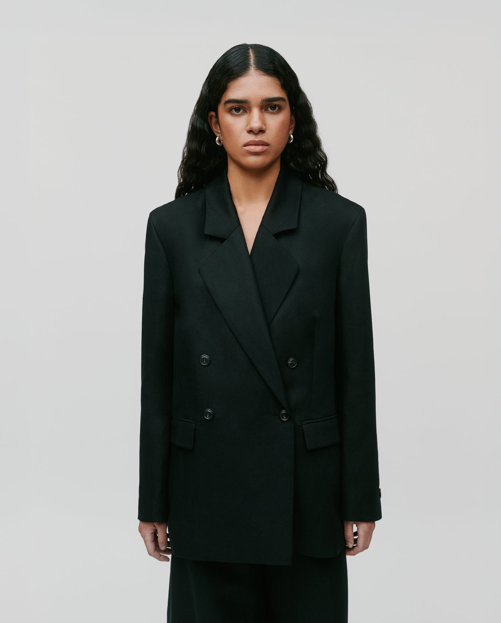 A person with long wavy hair wears the IVY OAK JASEMINA ROSE double-breasted blazer in black, standing against a plain background.