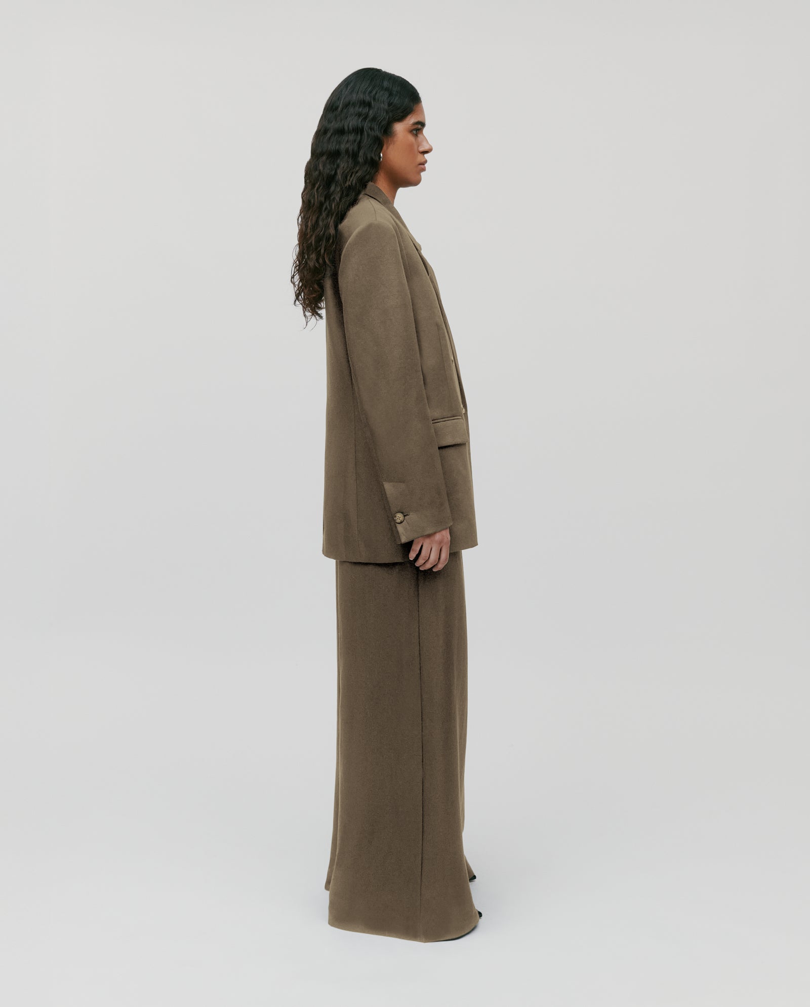 A person with long dark hair stands in profile against a plain light background, wearing the IVY OAK JASEMINA ROSE Blazer.