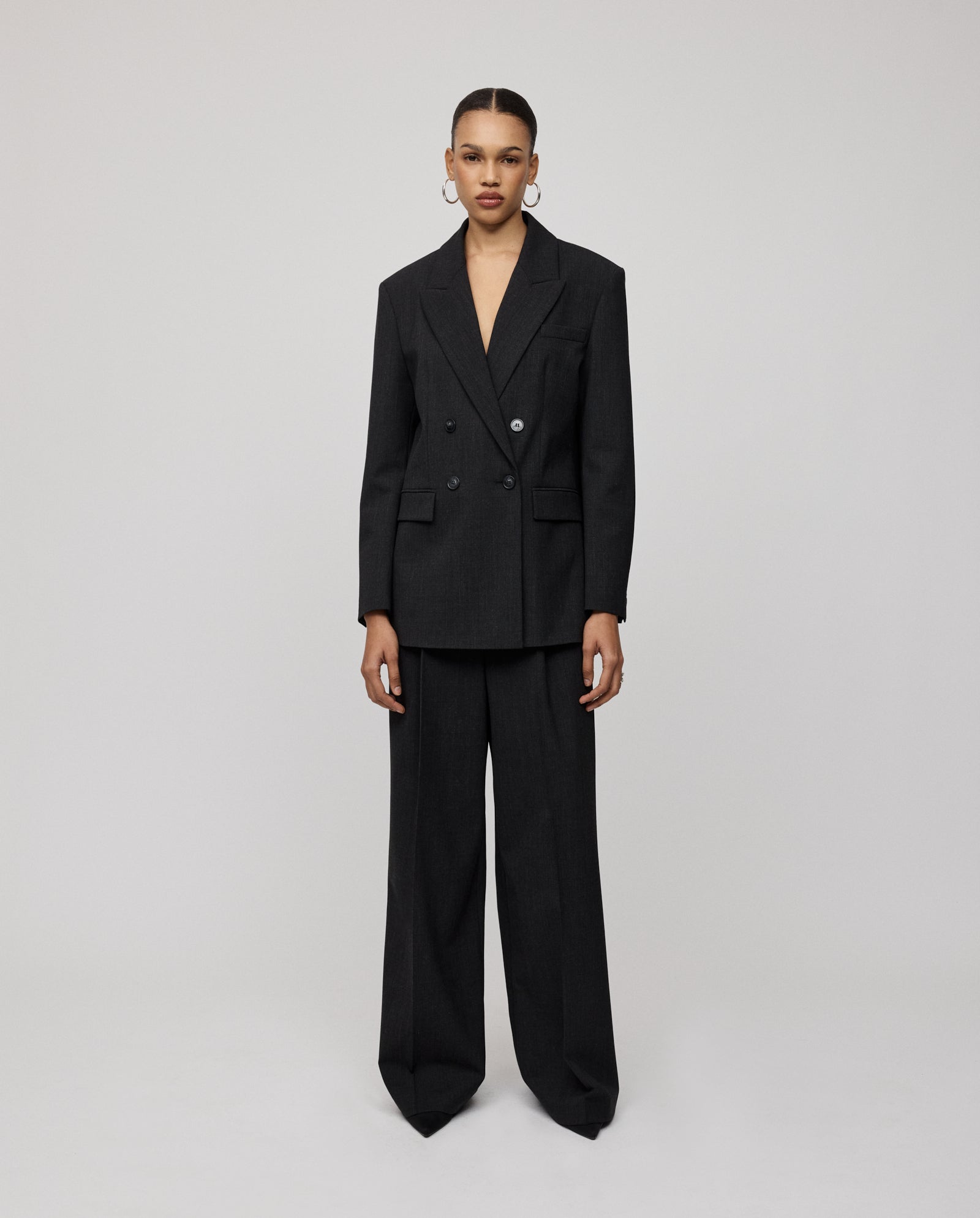A woman wears the IVY OAK JUDITH Blazer, a relaxed-fit, double-breasted black wool-blend twill pantsuit, standing against a plain light background.