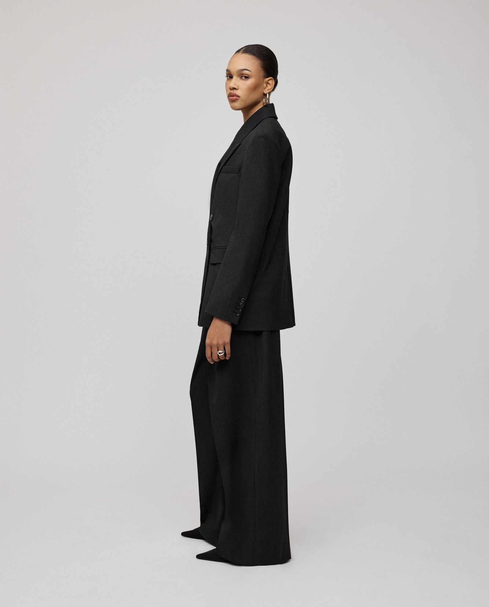 A person stands sideways against a plain light background, looking at the camera, wearing the IVY OAK JUDITH Blazer.