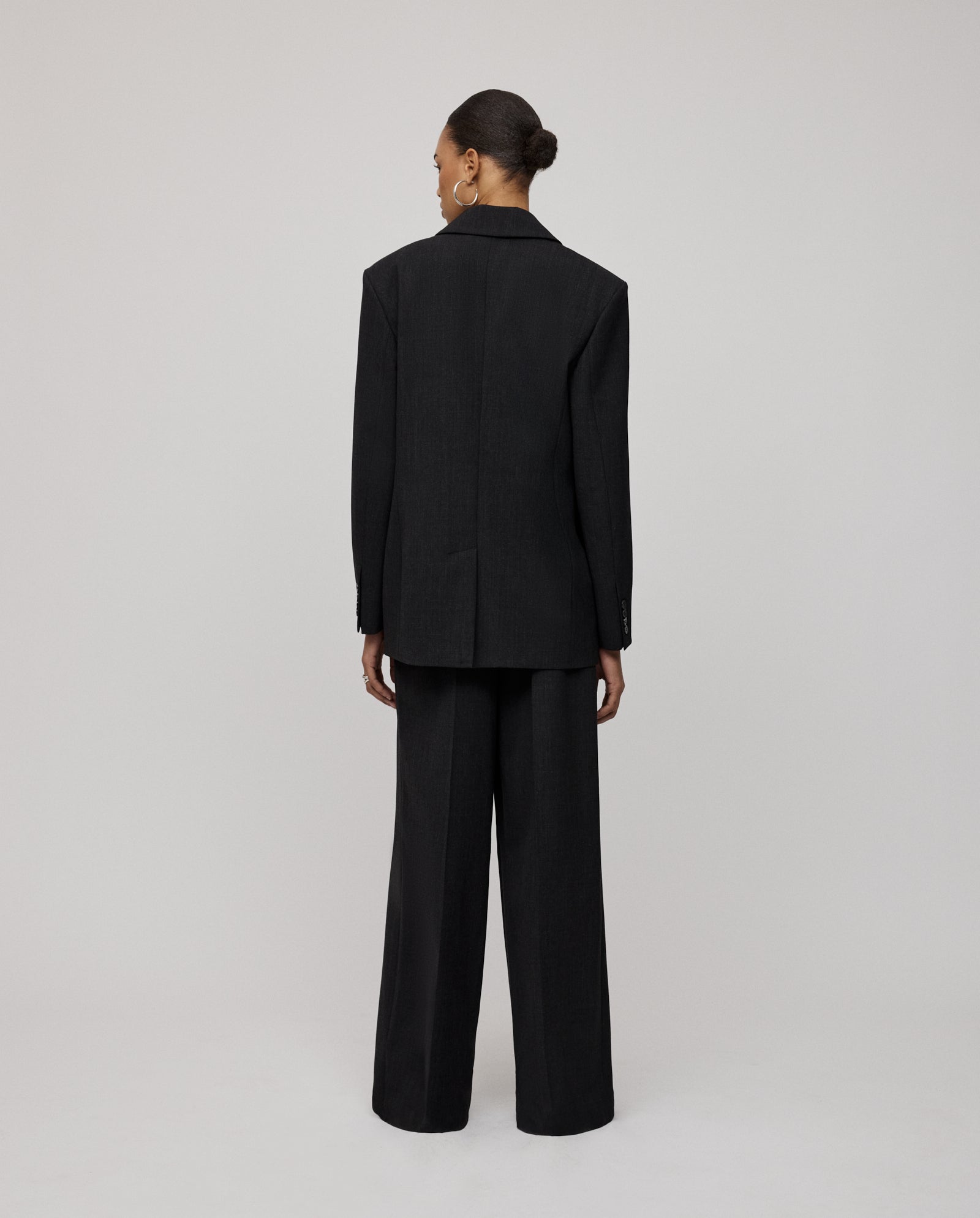A person in the IVY OAK JUDITH Blazer, featuring a black relaxed fit, stands facing away against a plain light gray background.